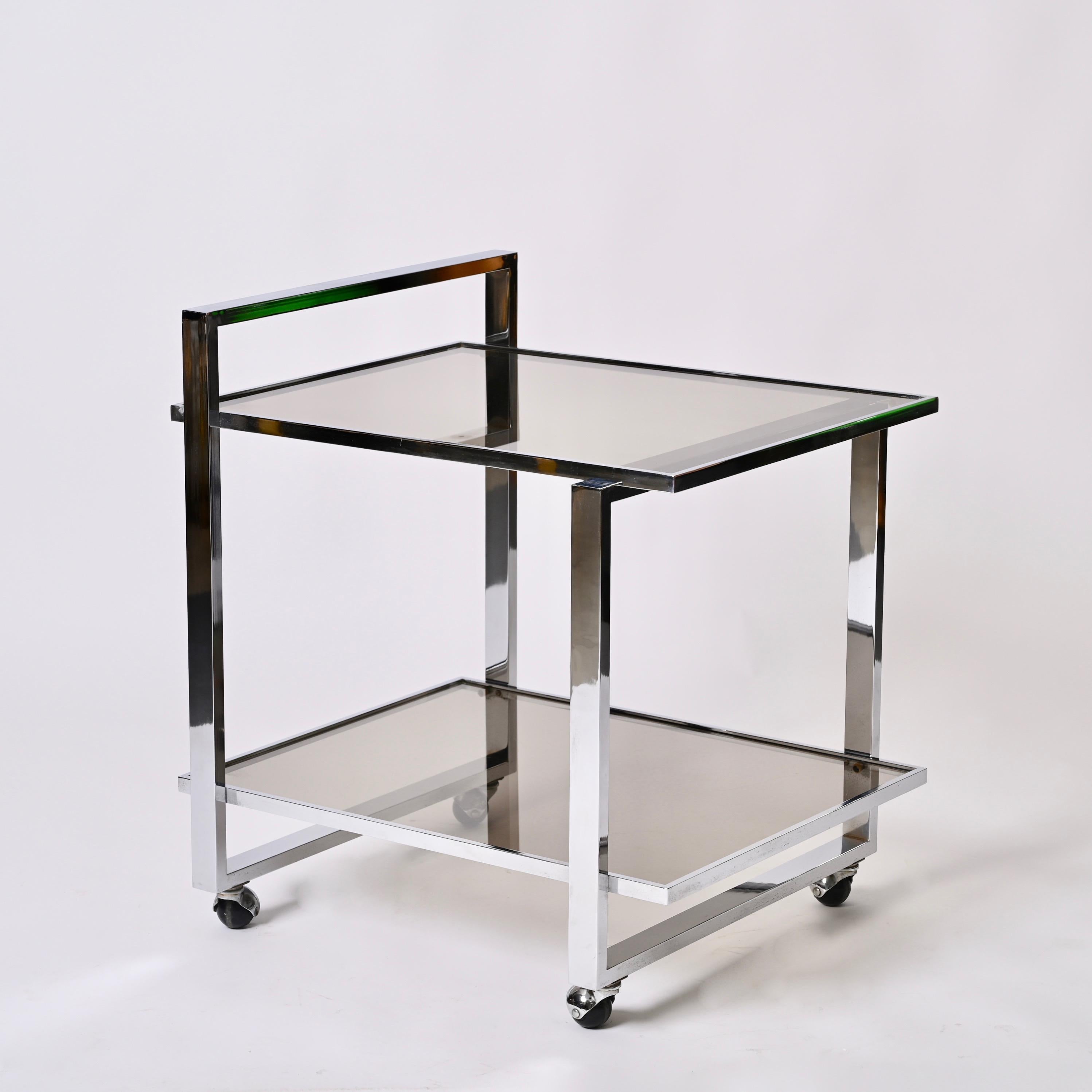 Beautiful midcentury bar cart in chromed steel and smoked crystal glass. This wonderful article was designed in Italy during the 1970s.

This piece is gorgeous as it has a shiny chrome frame structure with deep crystal glass trays. The two shelves