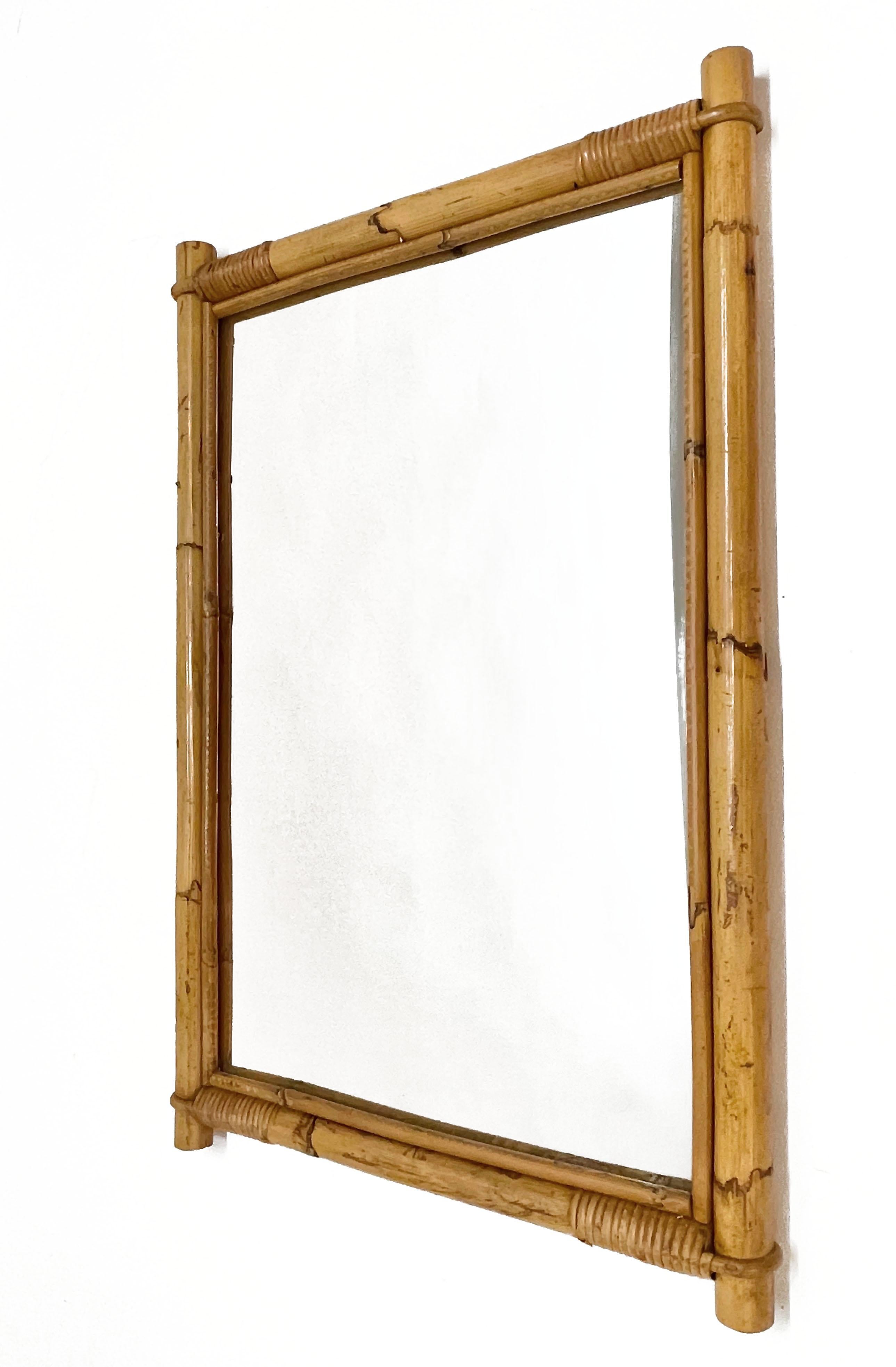 Wonderful midcentury rectangular mirror with a double bamboo cane weaved wicker frame. This amazing item was produced in Italy during the 1960s.

The way in which straight bamboo lines integrate with glass integrate is fantastic and coveys superb