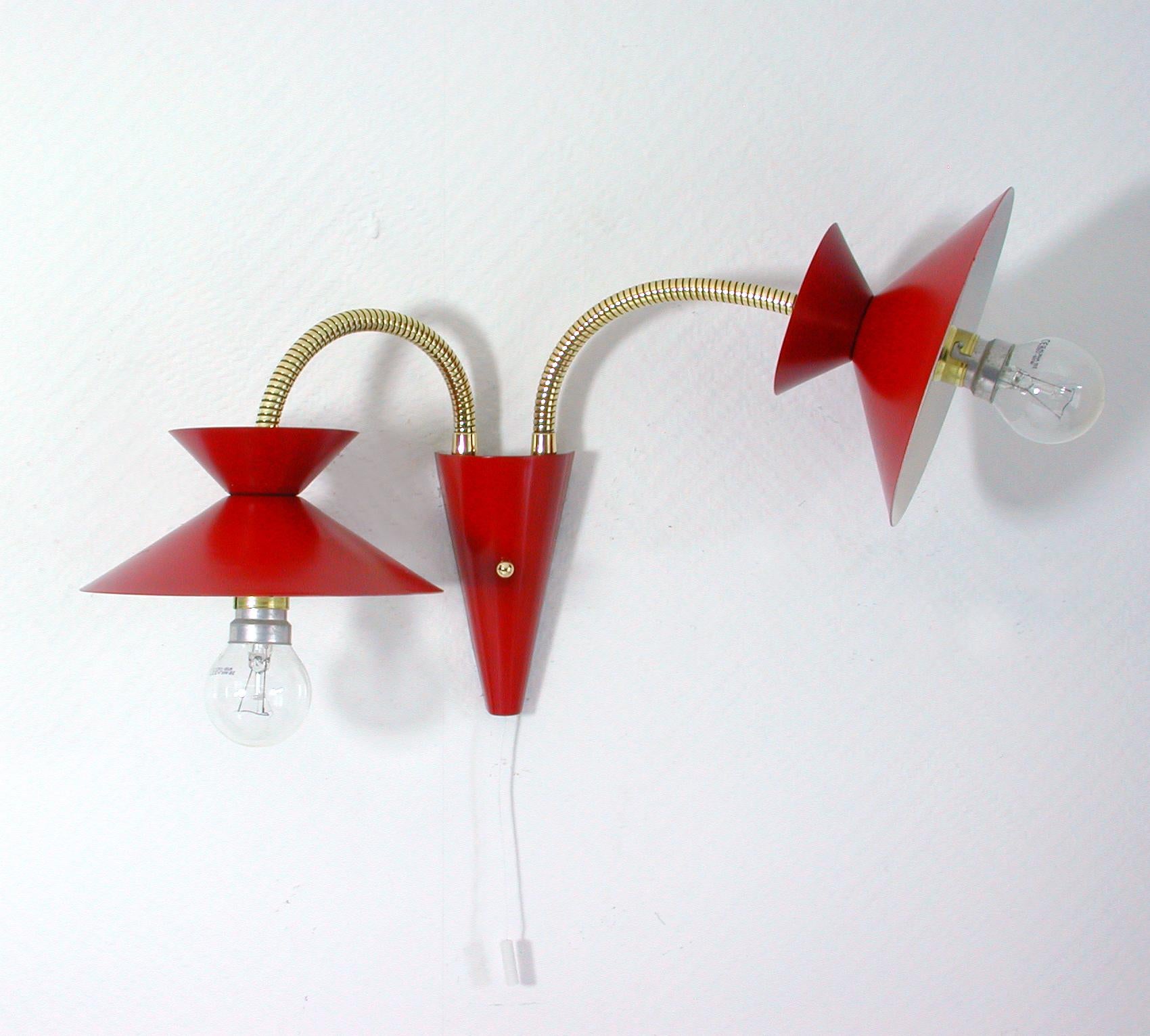 This elegant 1950s midcentury wall lamp / light fixture was designed and manufactured in France in the style of Pierre Guariche.

The wall light has got two red diabolo-shaped lampshades and brass gooseneck lamp arms. The lamp has been rewired.