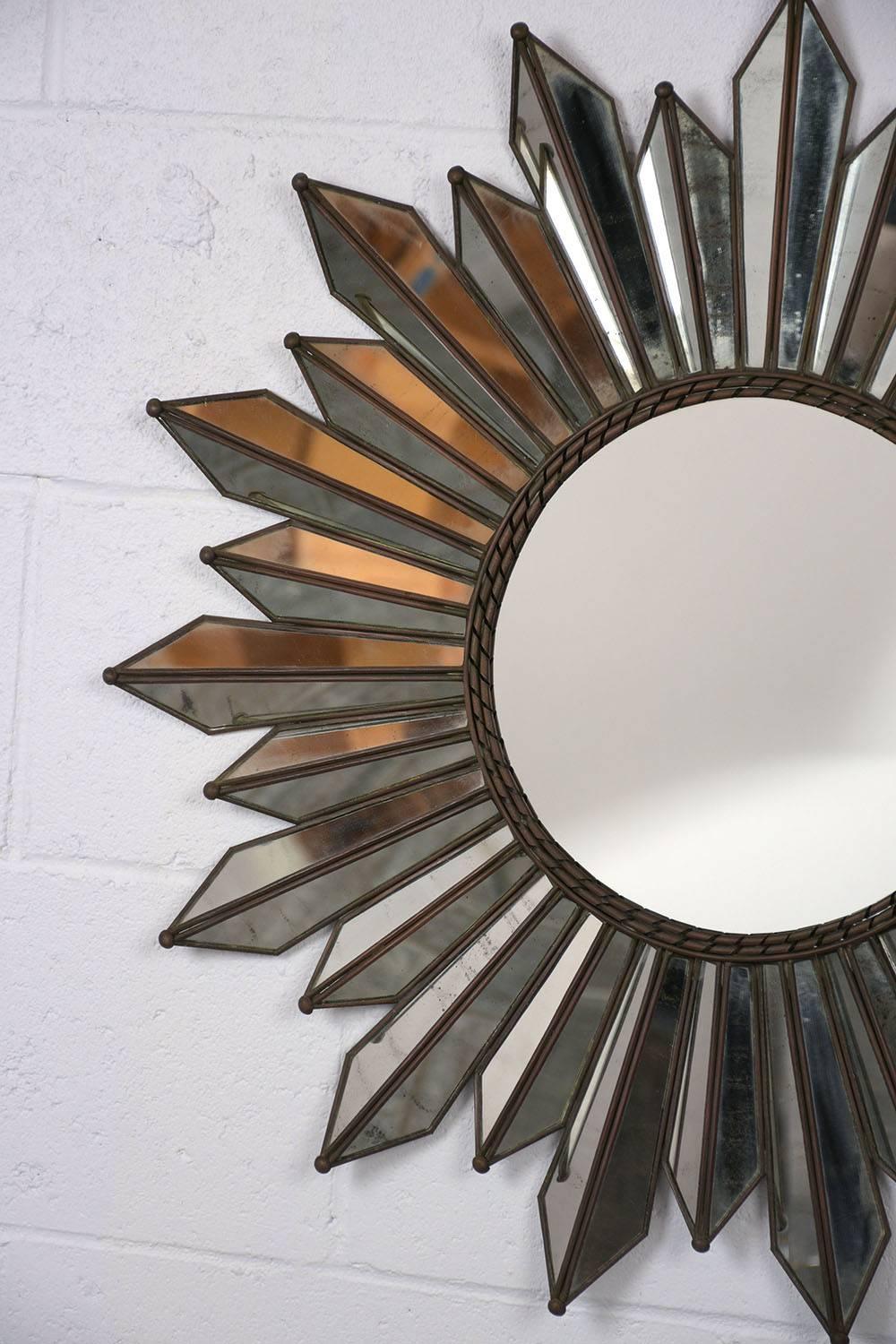 This 1950s Regency style sunburst mirror features a metal frame with geometric mirror accents at varying lengths. The centre mirror is fully reflective in great condition. Surrounding the centre mirror are two twisted metal band accents. This wall
