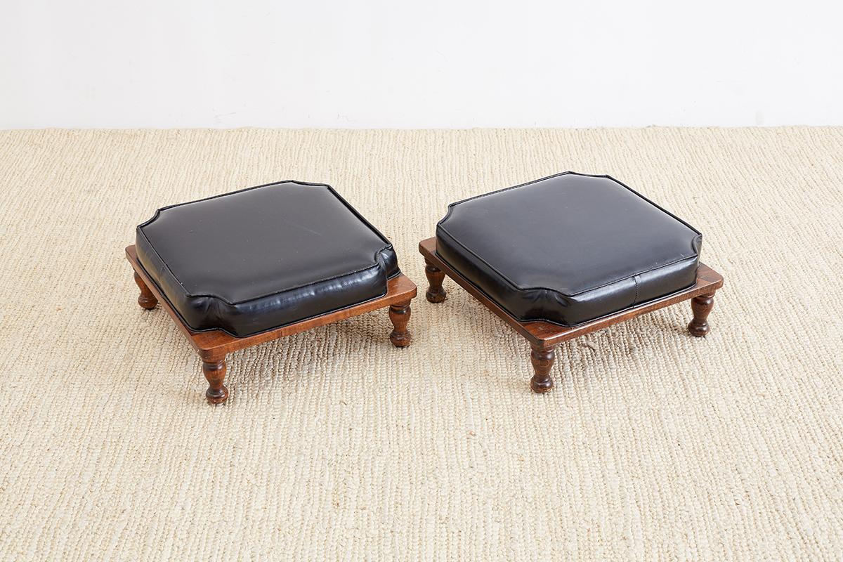 Pair of Mid-Century Modern stacking footstools by Ricardo Lynn. Made of mahogany and featuring a black faux-leather upholstered seat. Supported by small turned legs. These stools will stack on top of each other and legs fit into the notched corners.
