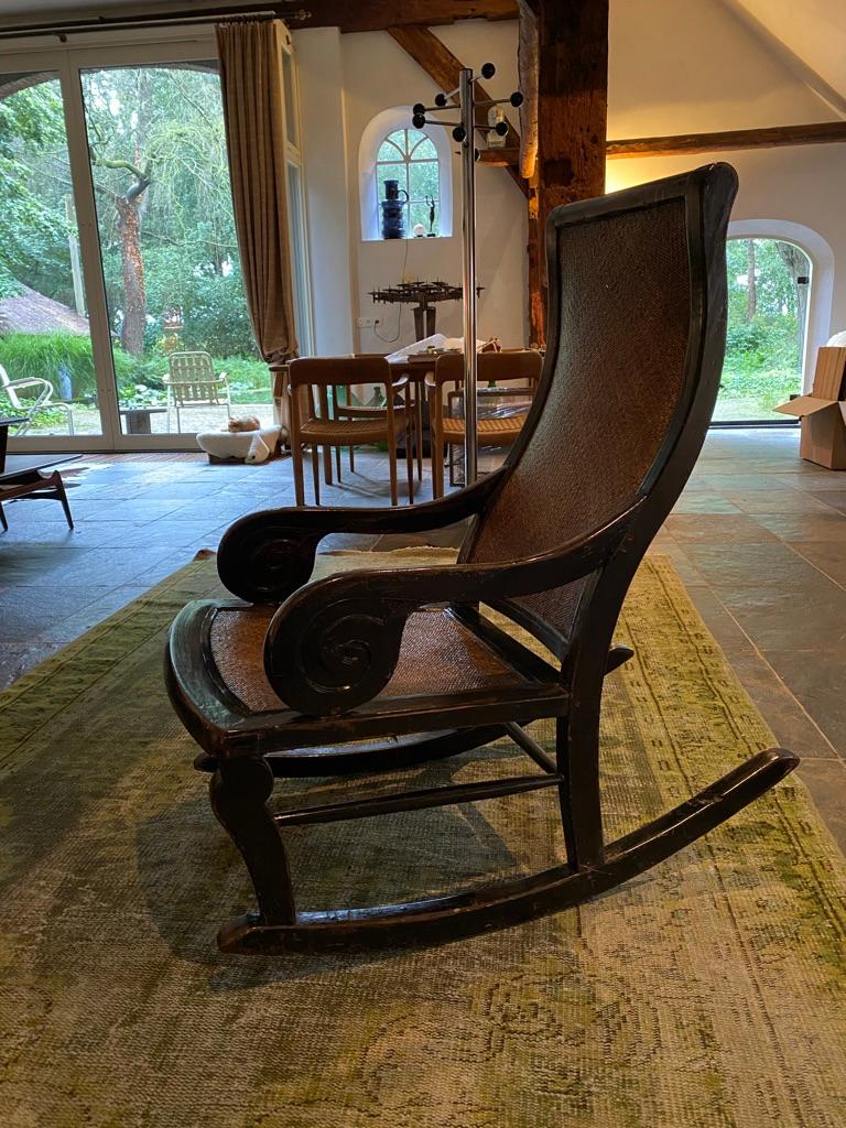 Midcentury vintage rocking chair, a blackened, polished hardwood frame and woven rattan back and seating.
Comfortable high back rocking chair. Shaped armrests terminate in spiral carved supports. The chair is good overal condition but has a very