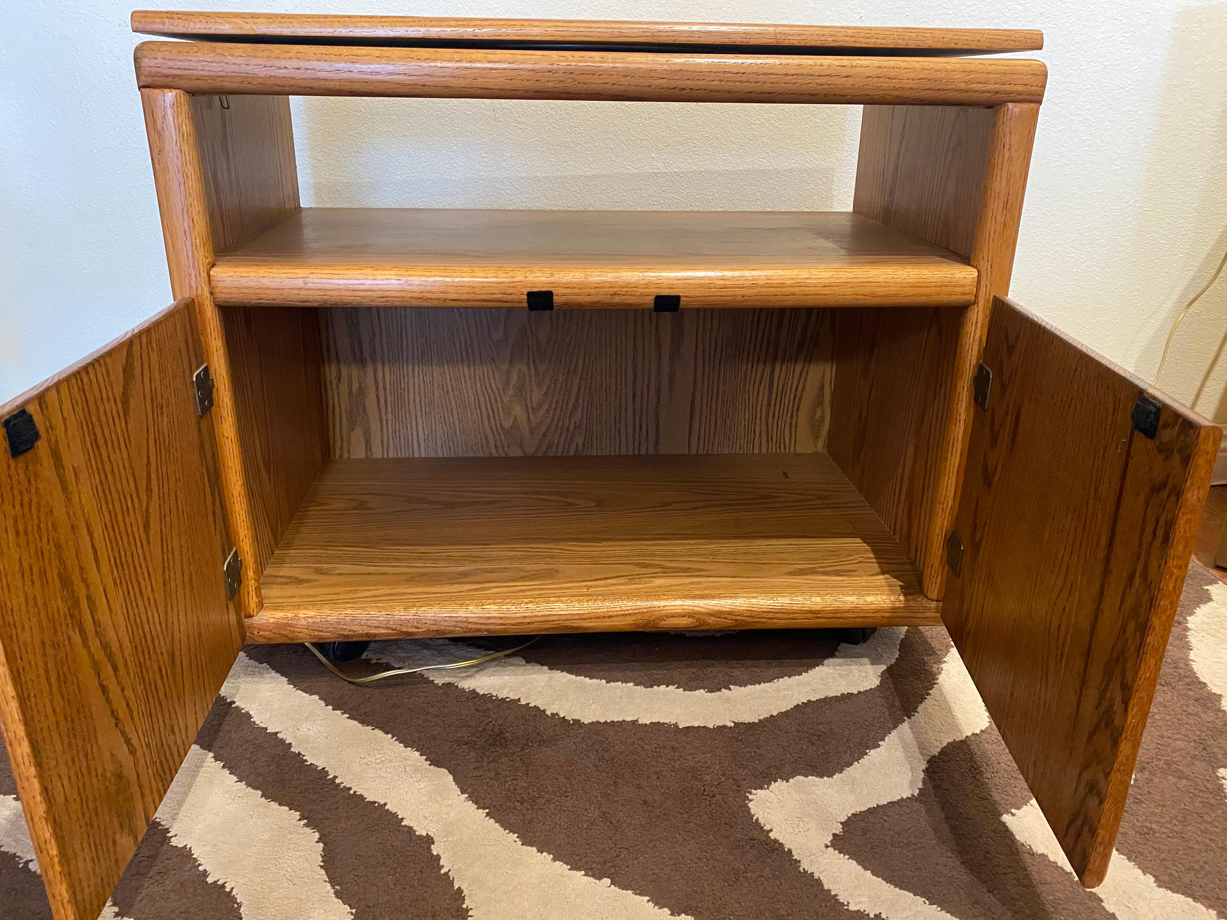 This mid-century rolling TV cabinet is made of walnut. It features a top section that pivots, allowing the television to be oriented in any direction. Below, there is an open compartment and two cabinet doors with carved handles in a classic