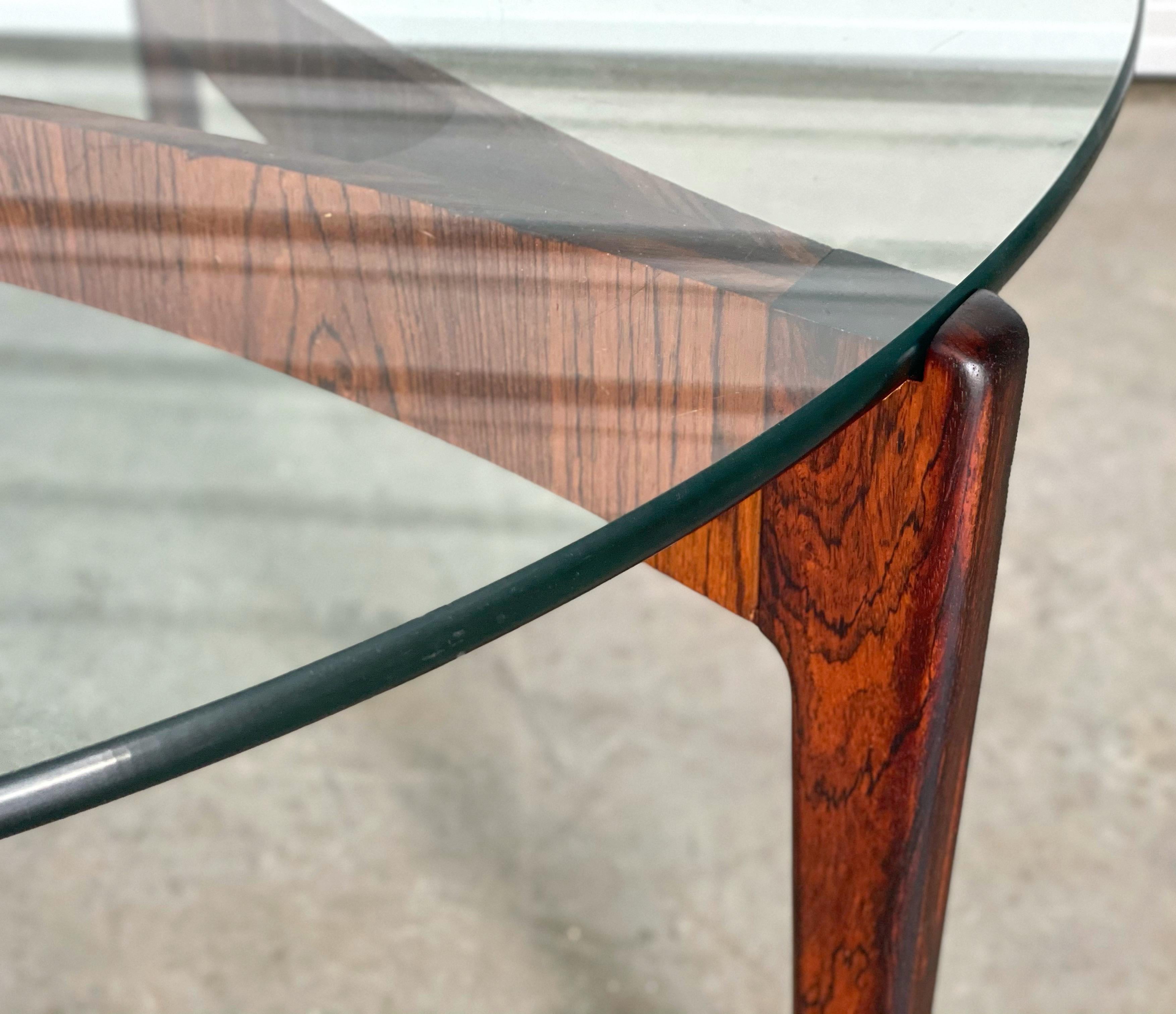 Danish modern circular cocktail table designed by Sven Ellekaer for Christian Linneberg Mobelfabrik, Denmark in 1962. This elegant piece is composed of a bent rosewood base featuring highly figured grain, supporting the original tempered glass table