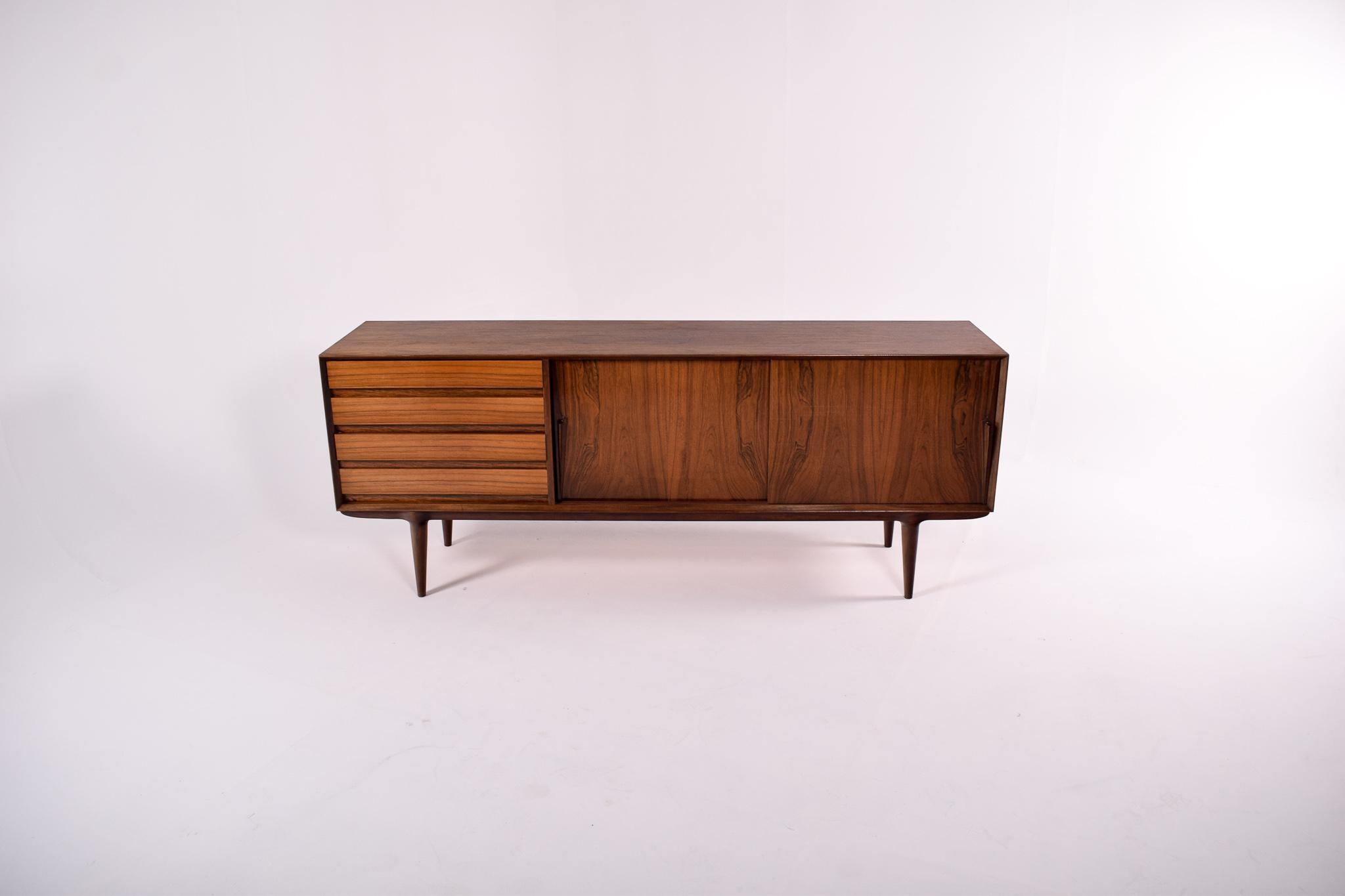 Designed by Gunni Omann in the 1960s, this sideboard conjugates the simplicity of the running doors with the drawers and the attractiveness of a beautiful veneer. The detail of the legs rounding size to receive perfectly the sideboard is also very