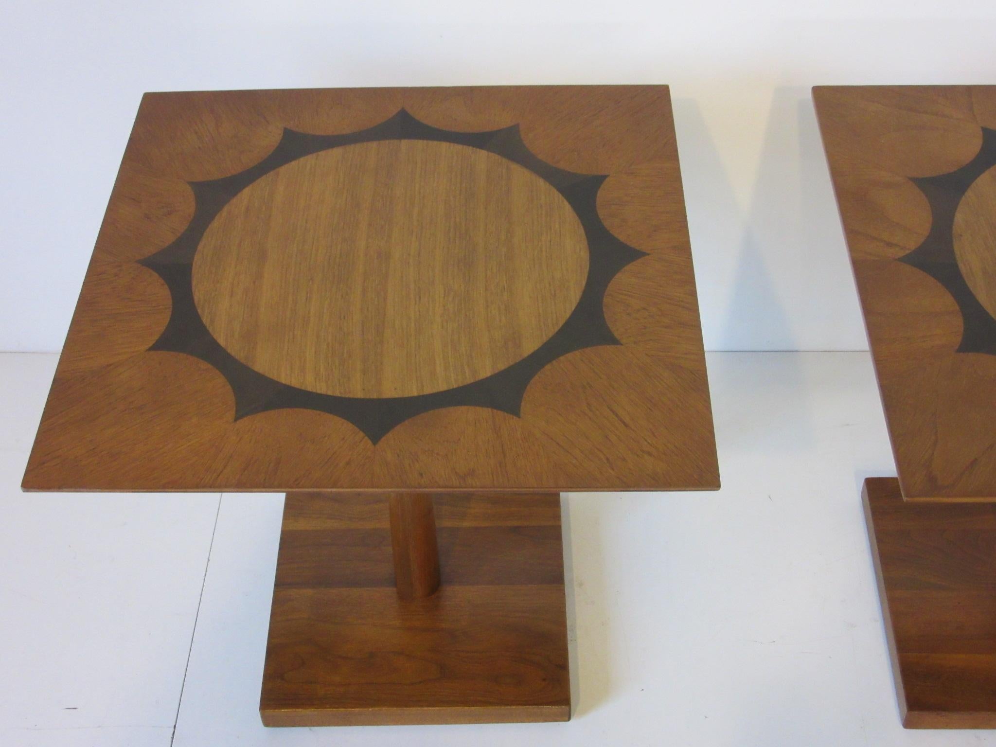 A pair of well crafted pedestal end tables in mahogany and walnut with a rosewood inlay design to the top, in the manner of the Baker Furniture Company.