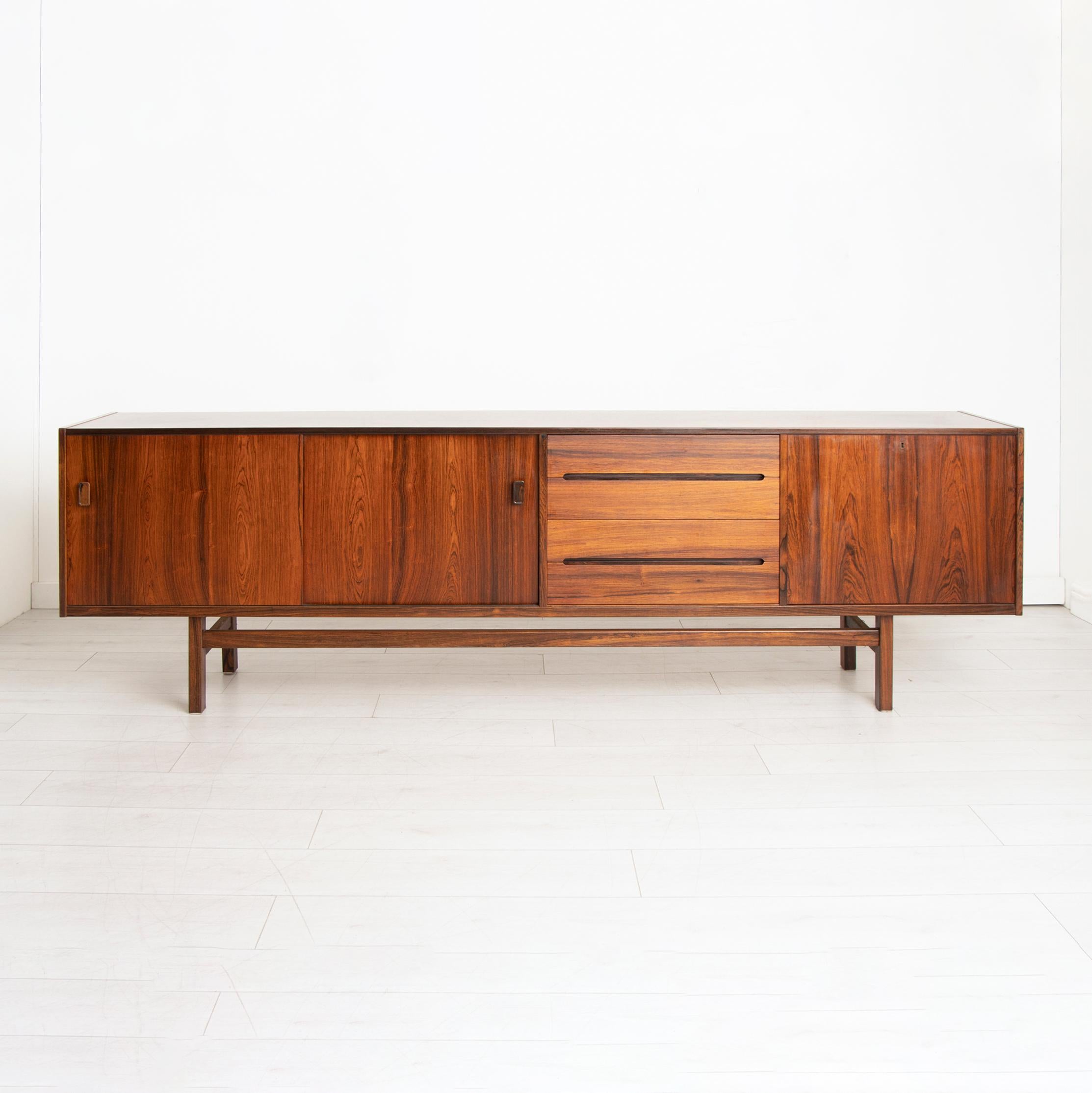 A midcentury long and low sideboard designed by Nils Jonsson for Troeds, Sweden. The sideboard is made in rosewood with two sliding doors with shelving behind, two drawers and a drop front bar.

Dimensions: W 253 x D 43 x H 78 cm.
