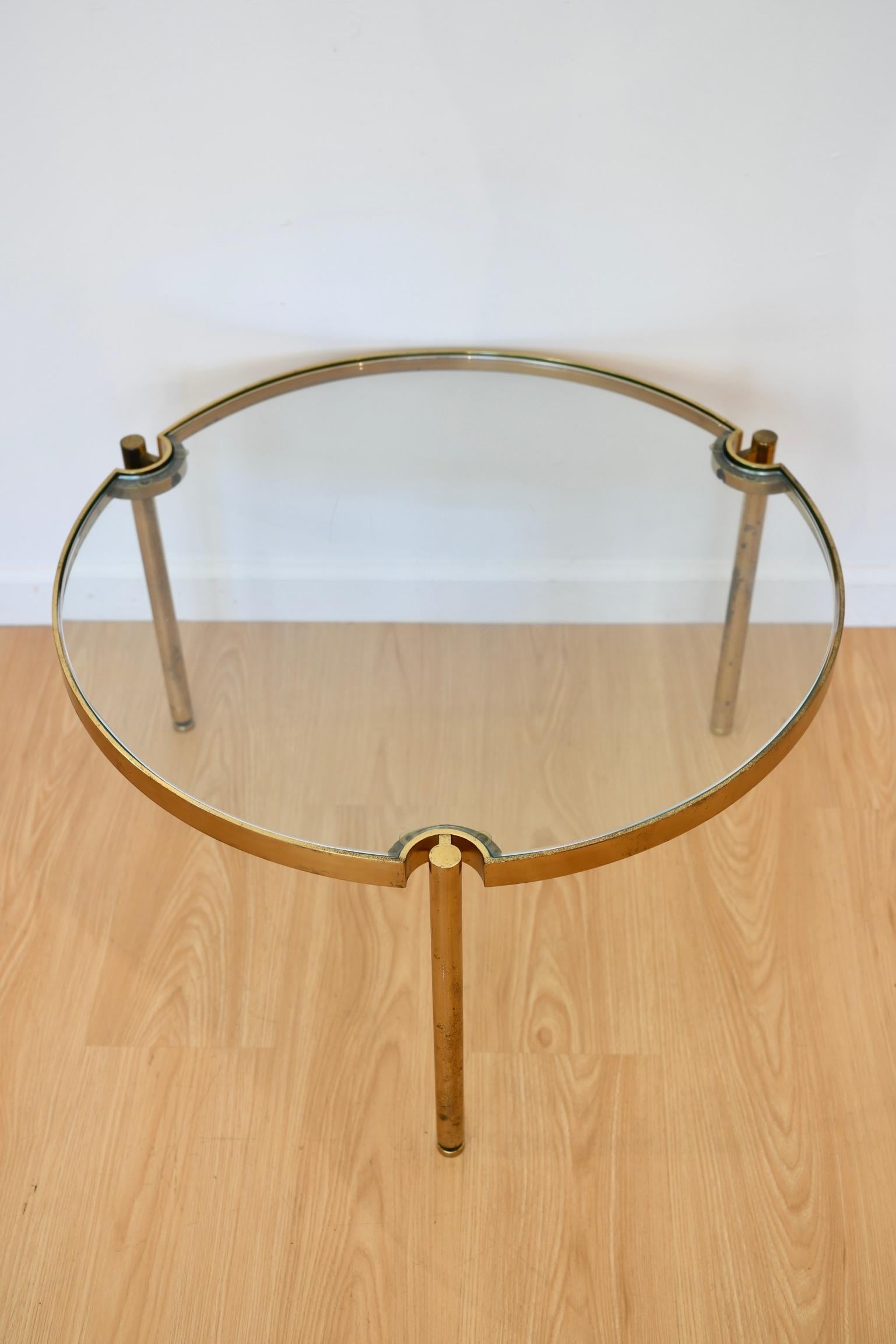 Table basse ronde à trois pieds en laiton avec plateau en verre. Quelques rayures sur le verre. Dimensions : 19 