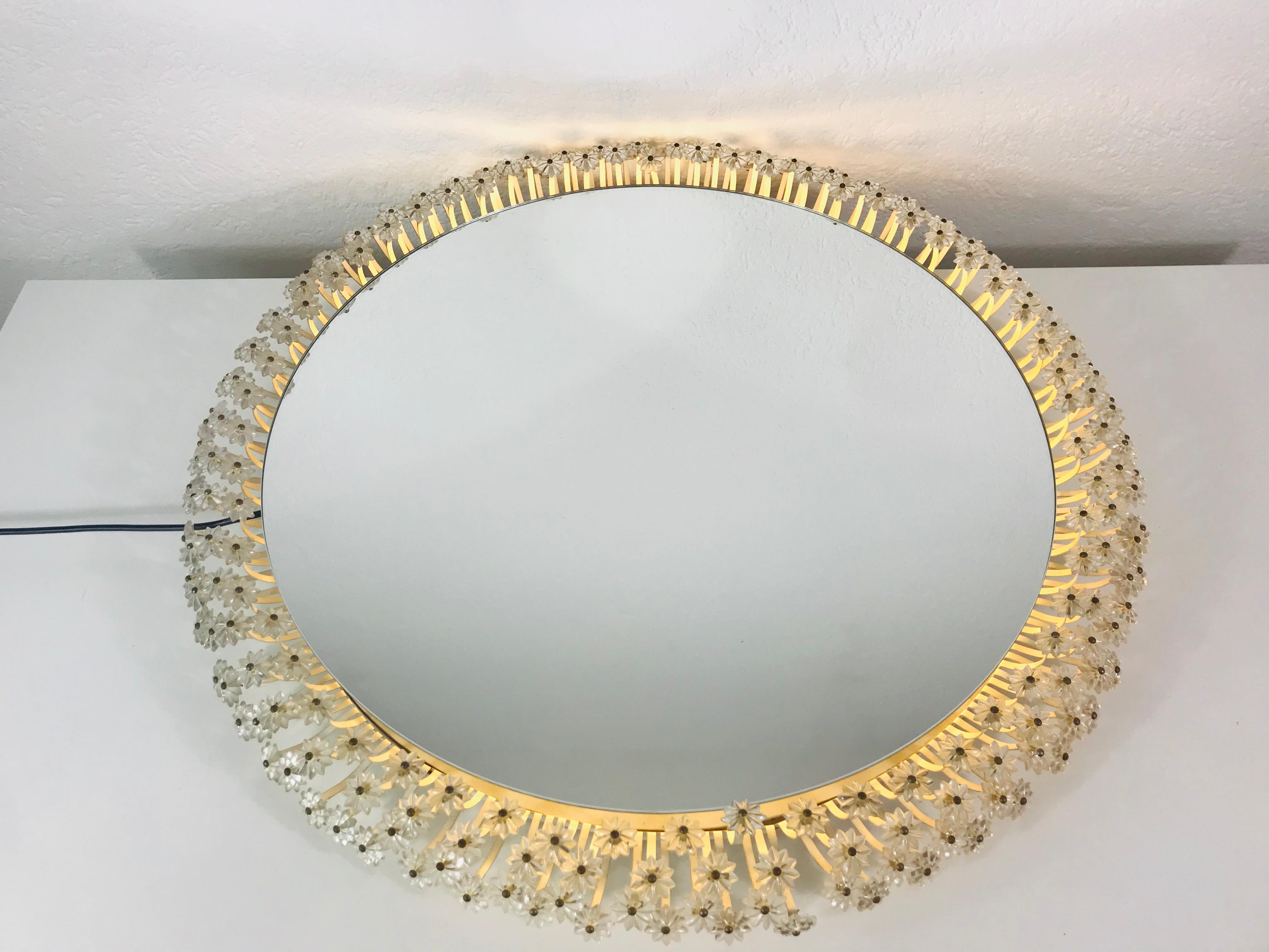 An illuminated wall mirror from the 1960s made in Austria. It was designed by Emil Stejnar for Rupert Nikoll. The mirror has a round design with beautiful acrylic flowers. There are E14 light bulbs inside the frame. The mirror is in a good vintage