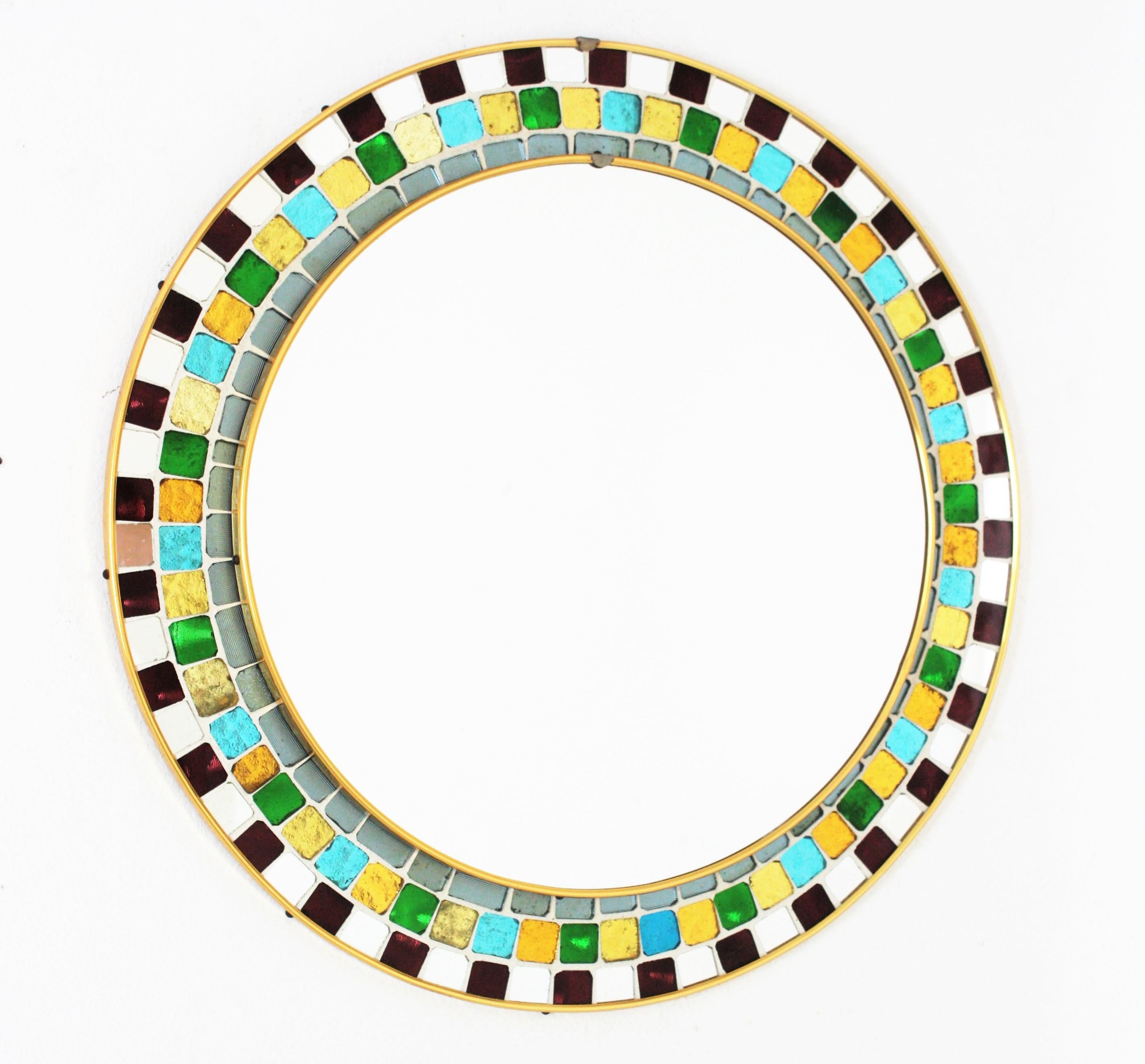Spanish midcentury mosaic round mirror framed with multicolor glass tiles. Spain, 1960s.
This gorgeous Mid-Century Modern mirror features a tile mosaic with small pieces of textured irisdiscent glass in different colors color cased on a white