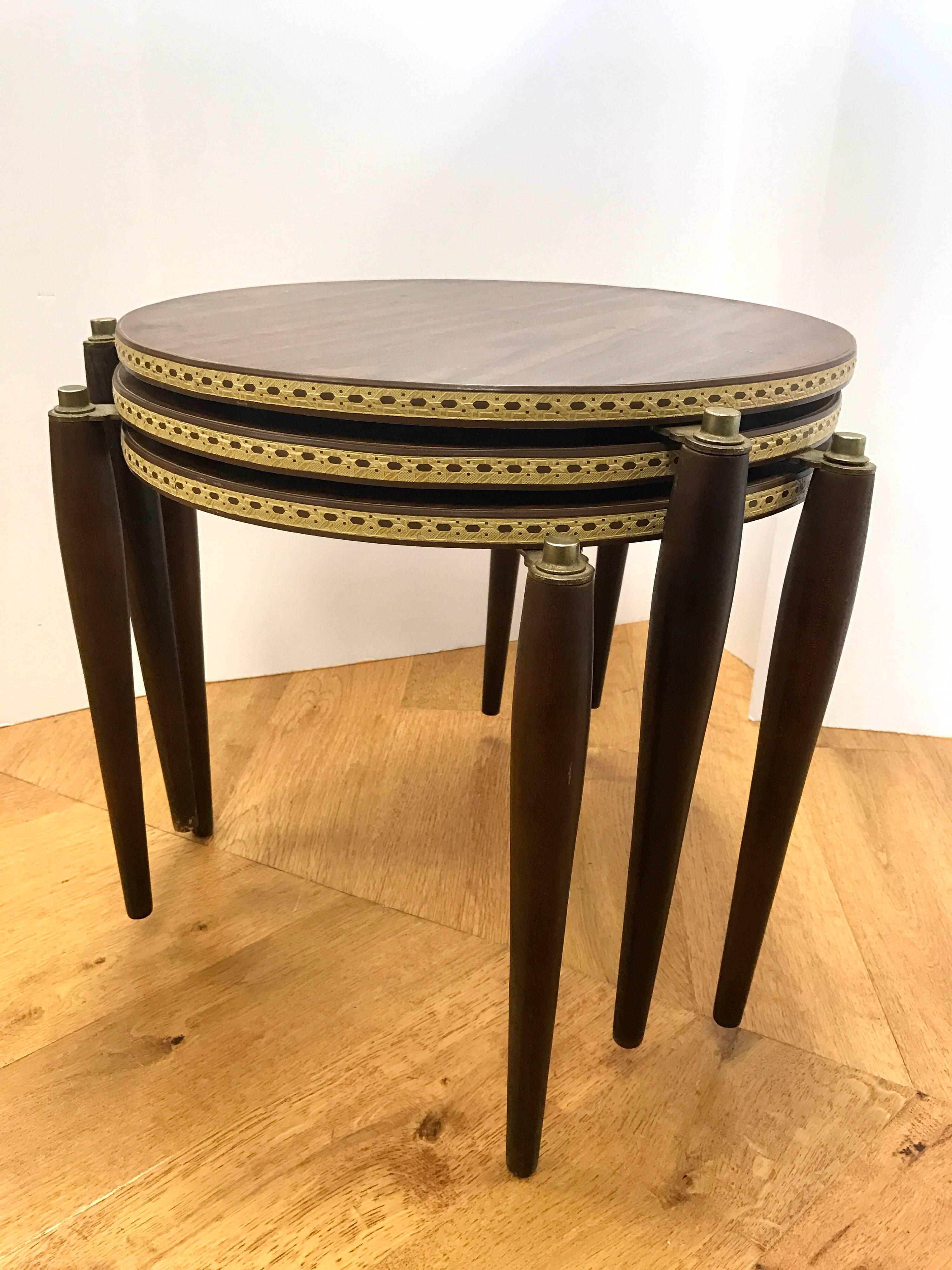 Beautiful set of three vintage modern nesting tables which feature circular wood laminate tops, formica on the bottom side and gorgeous tapered legs secured with gold caps. Unique tabletop sits on a tripod base with brushed metal feet. Versatile