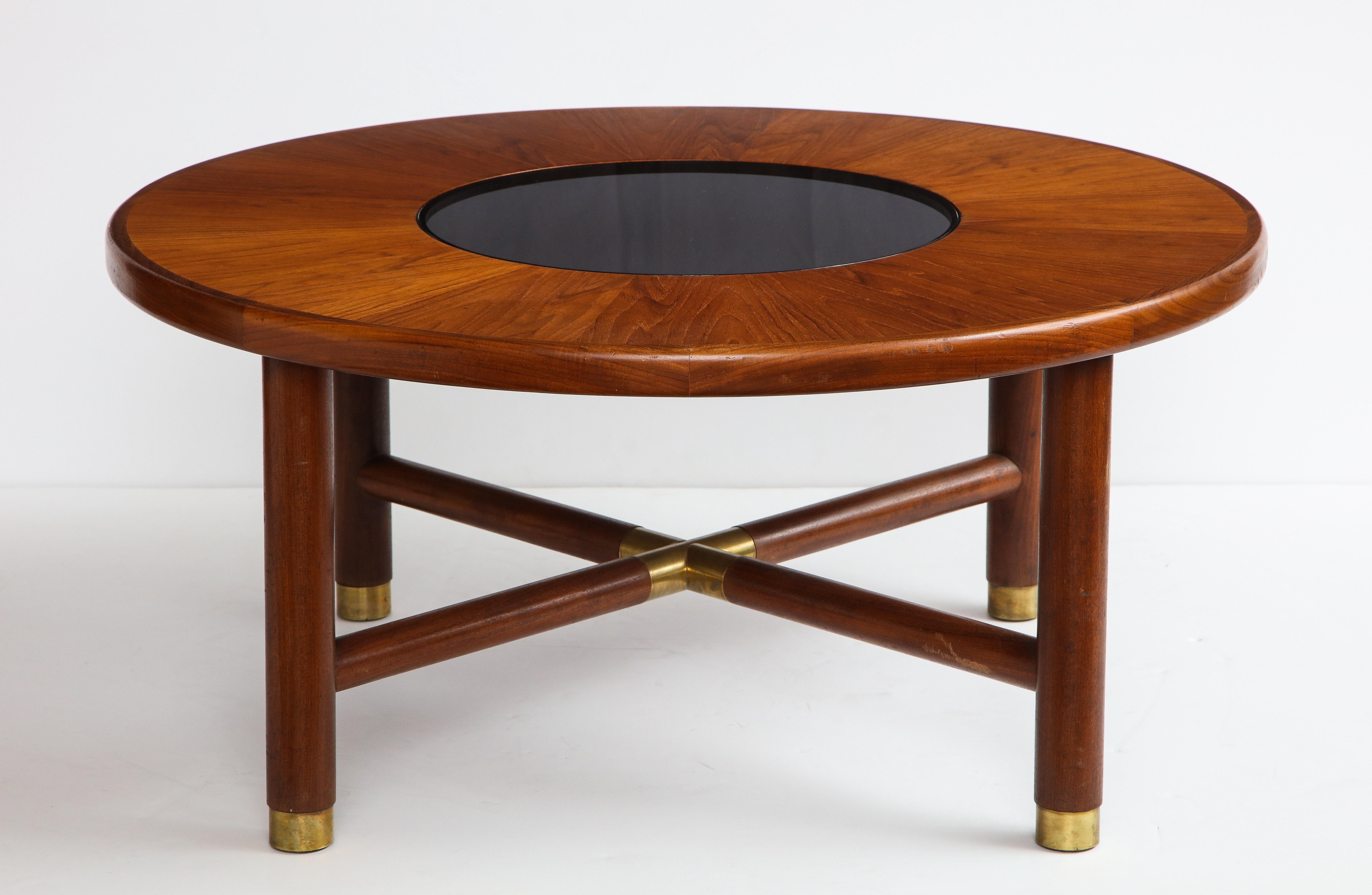 Midcentury round teak and smoked glass coffee table, United Kingdom, made by G-Plan Furniture in the 1960s. Cherry wood veneer, teak wood base with patinated brass accents and sabots. Surface scratches on the brass feet. Dark smoked glass center