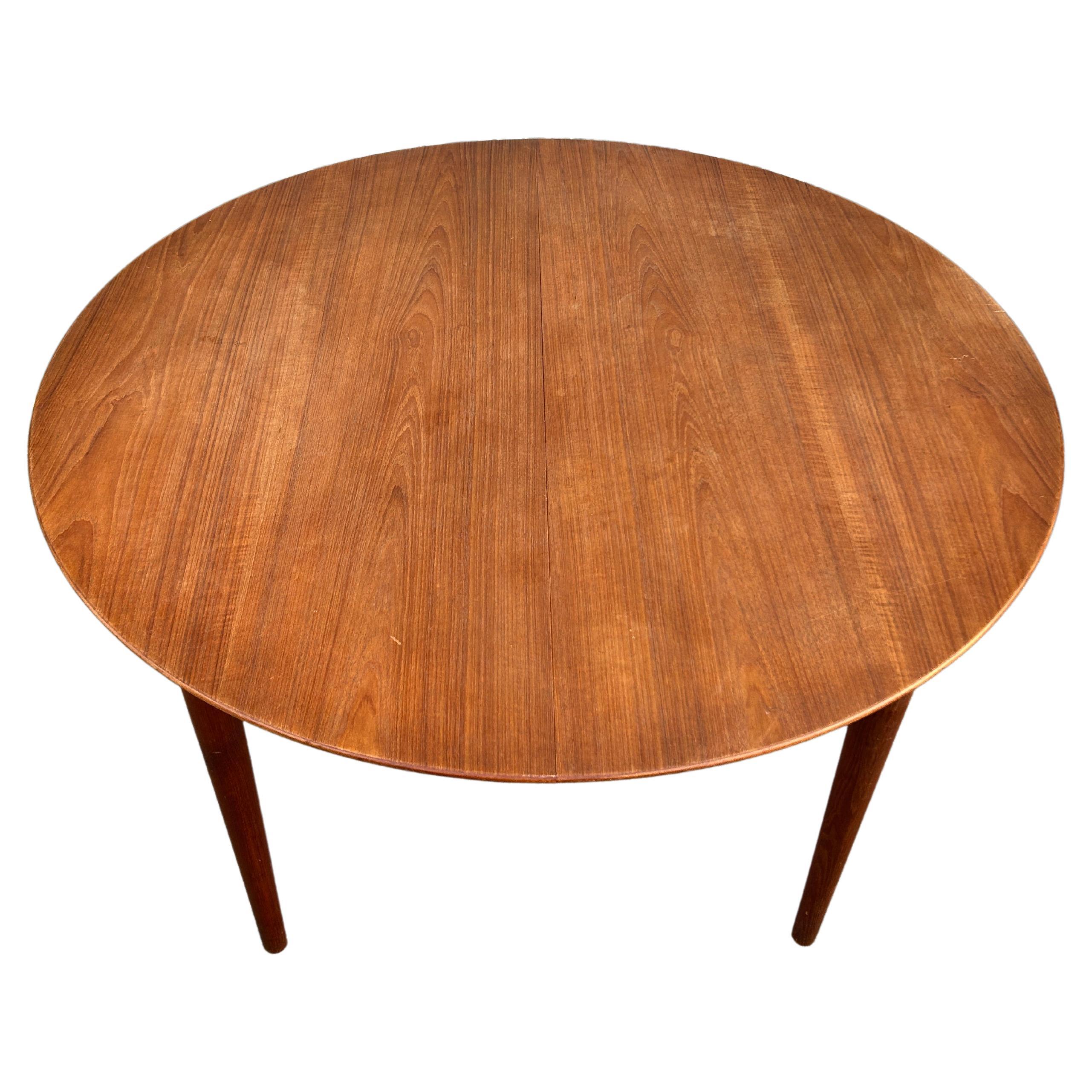 Mid century teak round Danish Modern extension dining table with (2) leaves. This table has Solid teak legs that unscrew with bolts. This table is in good vintage condition shows signs of use, both leaves match the table 100% and have aprons.
