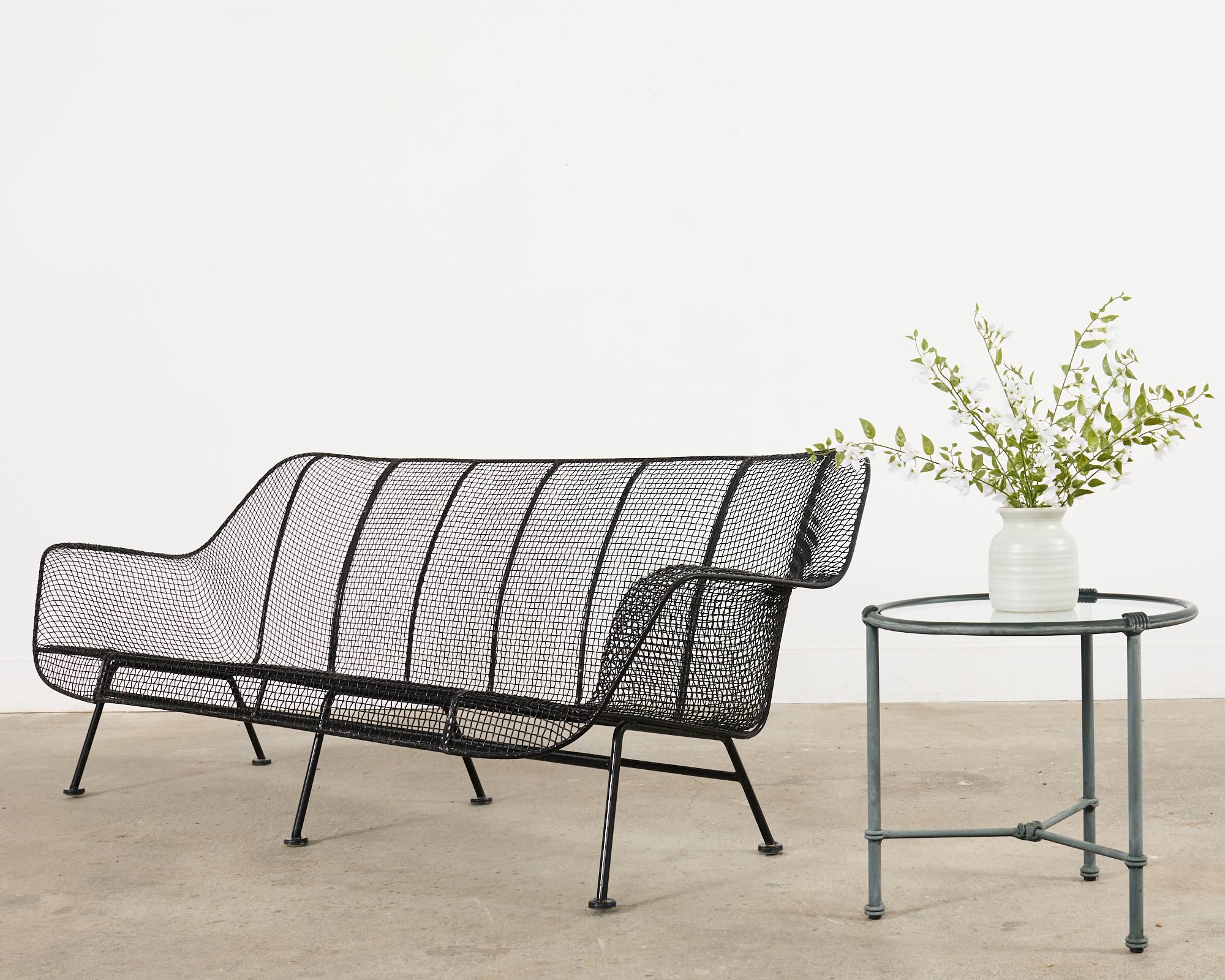 Iconic mid-century modern Sculptura patio and garden sofa crafted from wrought iron and wire mesh by Russell Woodard. The gracefully curved sofa has a thick wrought iron frame that is covered with fine wire mesh having a black powder coated finish.