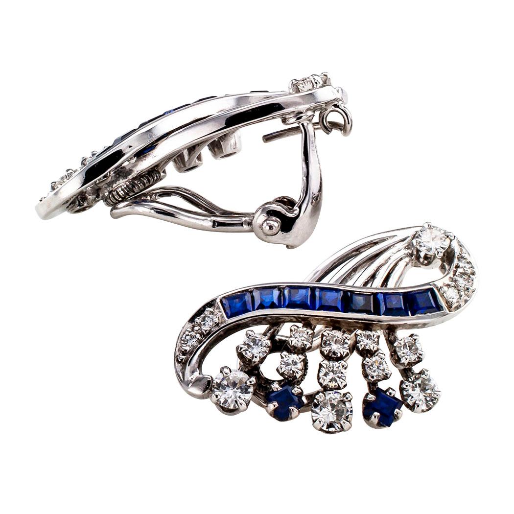 Mid Century sapphire diamond and white gold ear clips circa 1950. The matching designs feature scrolling ribbons set with calibrated sapphires and round diamonds, supported by radiating sprays set with additional diamonds and sapphires, the eighteen