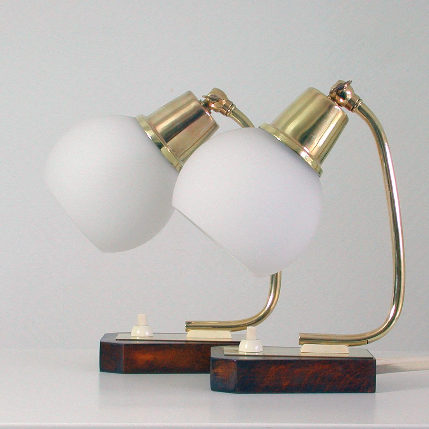 These vintage midcentury table lamps were made in Denmark in the late 1950s. They are made of brass, have got wooden (teak?) bases and adjustable opal glass lamp shades.