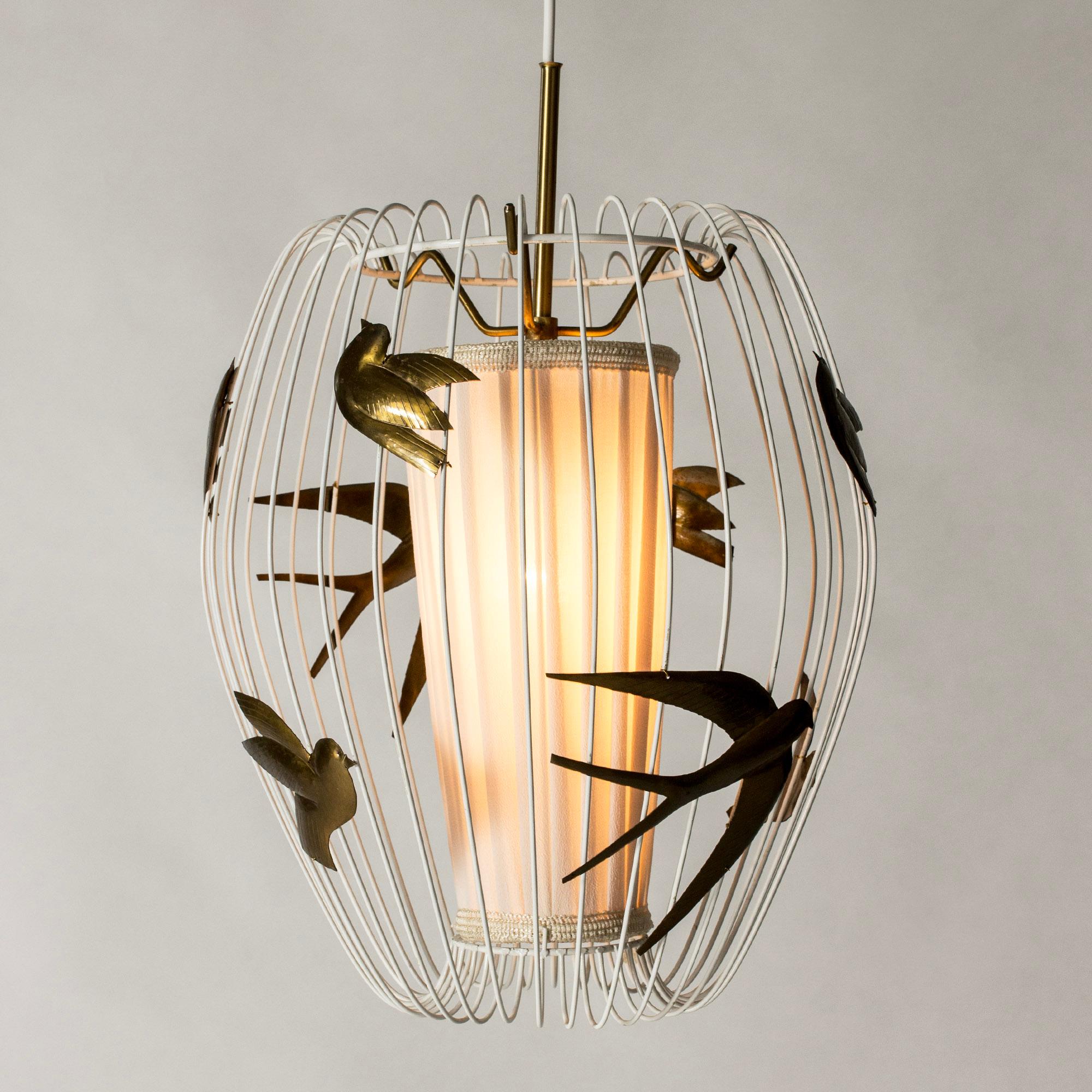 Wunderschöne Pendelleuchte von Hans Bergström in voluminösem Käfigdesign. Weiß lackiert mit einem Dekor aus applizierten Messingschwalben und Gartenvögeln. Lichtquelle mit weißem Stoff abgeschirmt.

Hans Bergström war Inhaber und kreativer Leiter