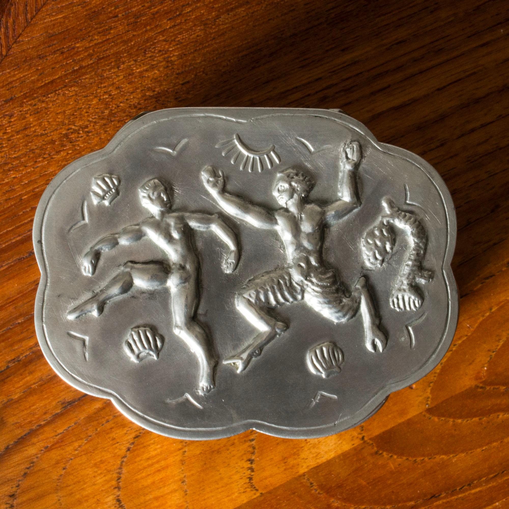Lovely pewter box from Herman Bergman, in oval shape with a scalloped silhouette. Decor of a lively woman and a faun among shells and coral. Pretty etched pattern on the lid and around the base.