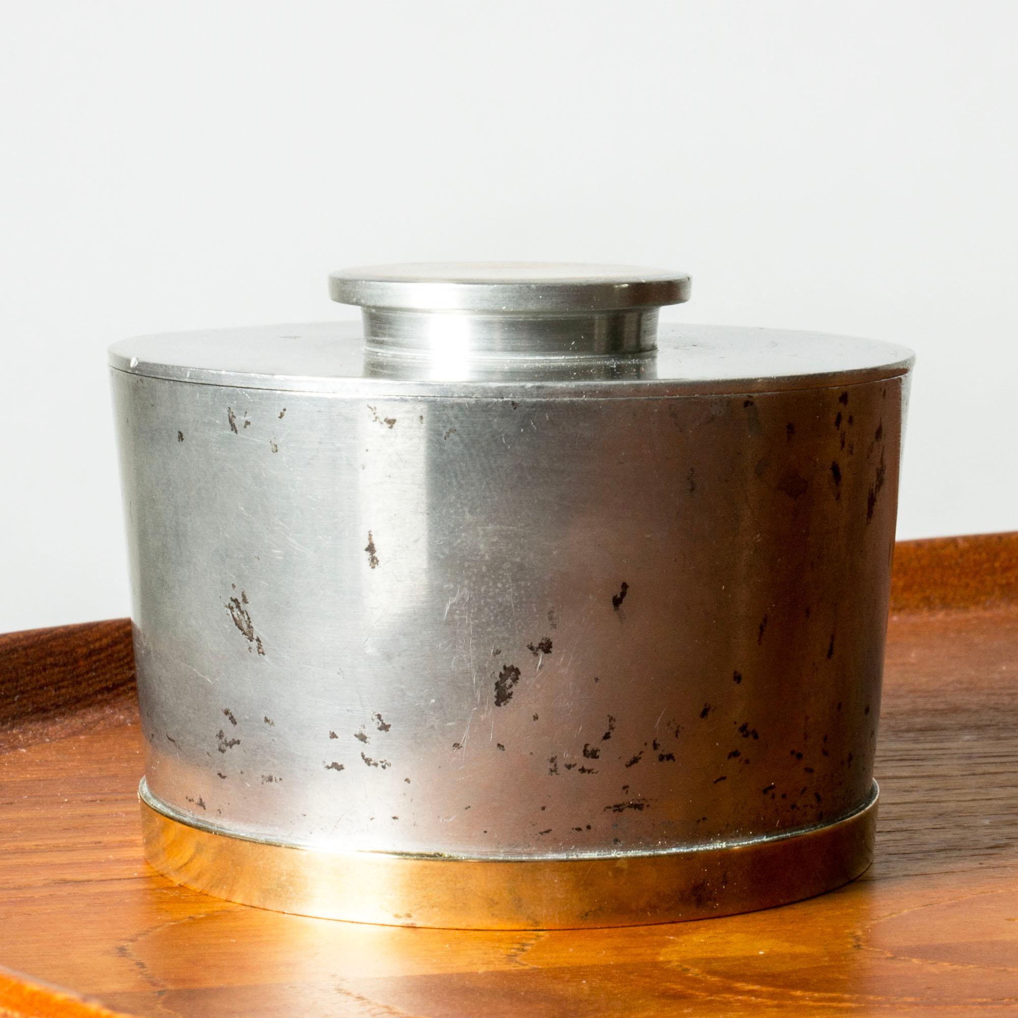 Sleek pewter jar by Nils Fougstedt, in a compact form. Knob made partially from brass, decorative brass rim around the base.