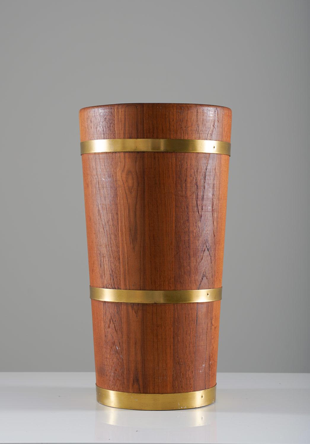 A stately and practical umbrella stand, constructed of solid and durable teak wood, enhanced by brass rings, is a functional and stylish addition to any entryway or foyer. The rich natural tones of the teak wood and the warm gleam of the brass