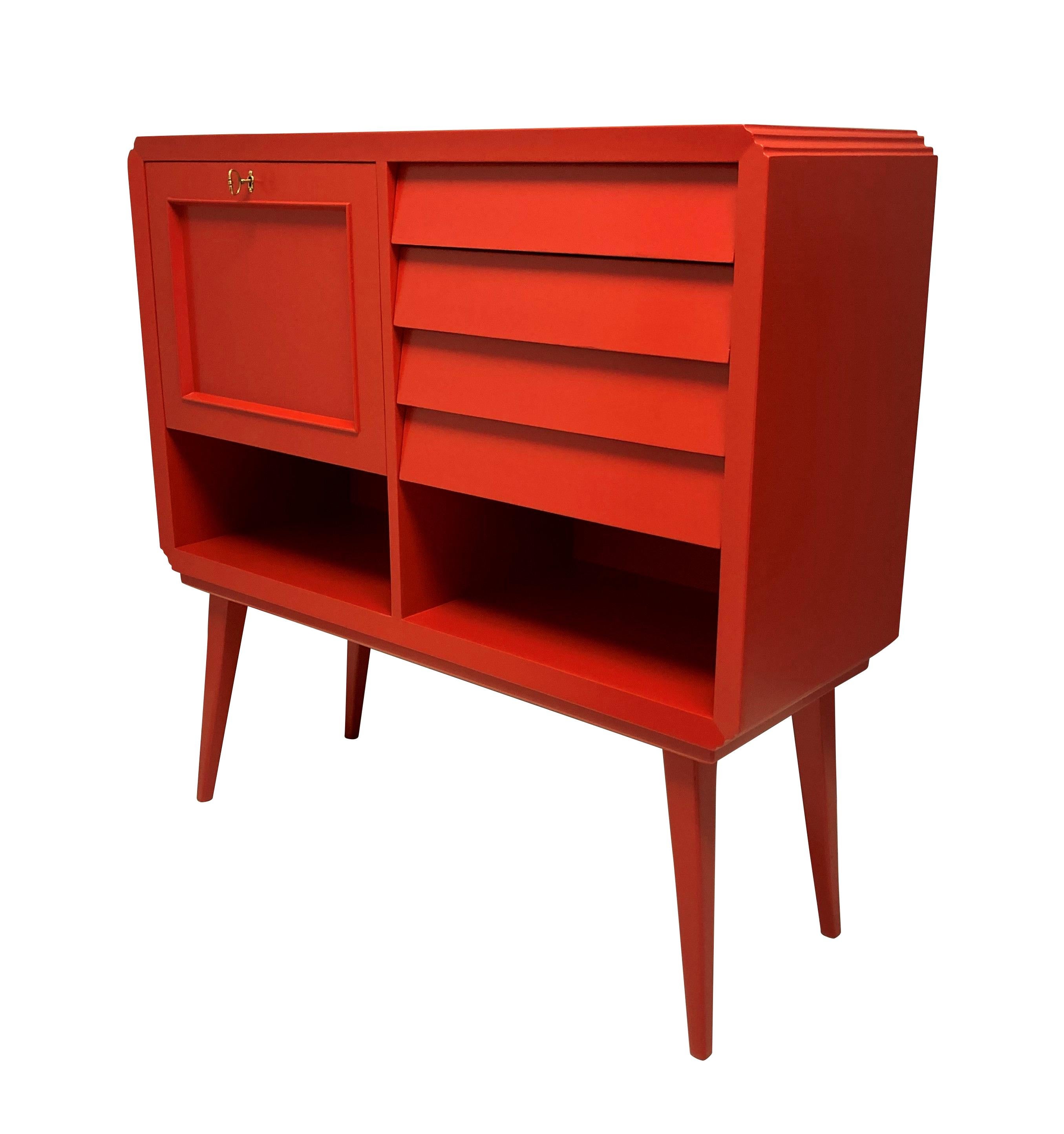 A striking Italian Mid-Century scarlet lacquered bar cabinet, with four angled drawers, two lower compartments and the bar, mirrored inside with a glass shelf.