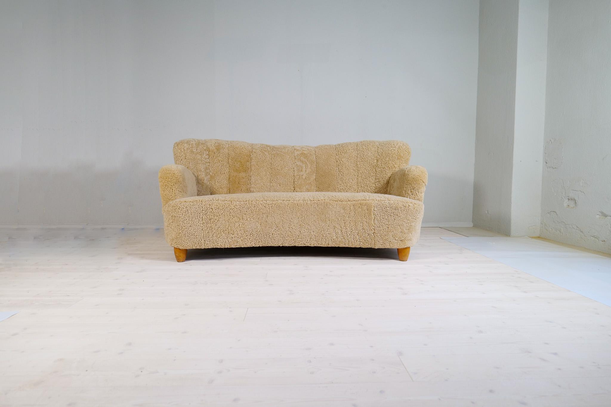 This sculptural sofa with its curvy frame was produced in the early 1940s. The sofa has been fully reupholstered and now have its beautiful light brown / honey sheepskin/shearling. The structure and legs are made in polished birch with wonderful