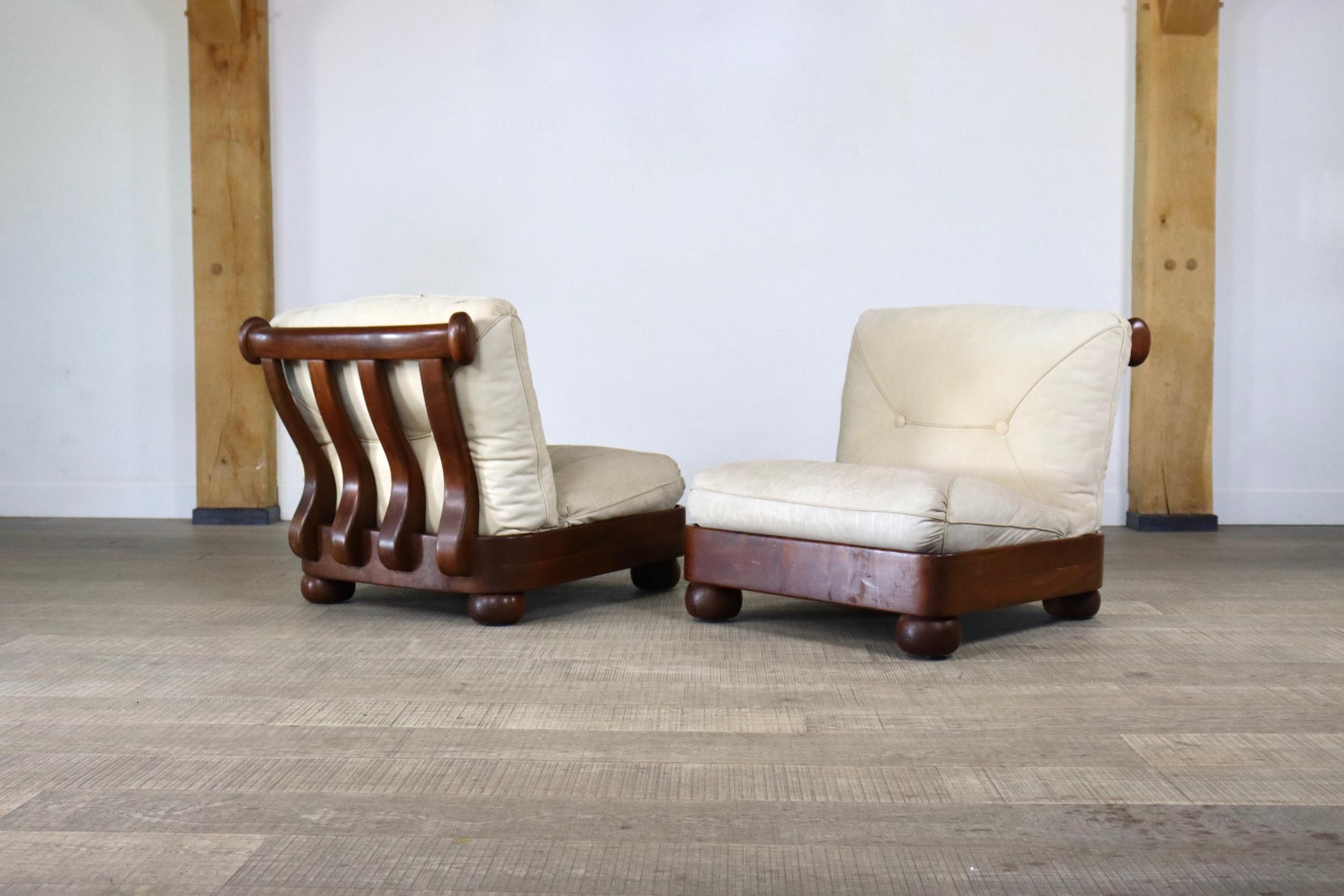 Incredible pair of sculptural lounge chairs from Italy 1960s. The stunning solid wooden frame is supported by thick round legs that have built in wheels. This way it is very easy to move them around. Complementing the frame are two chunky cream
