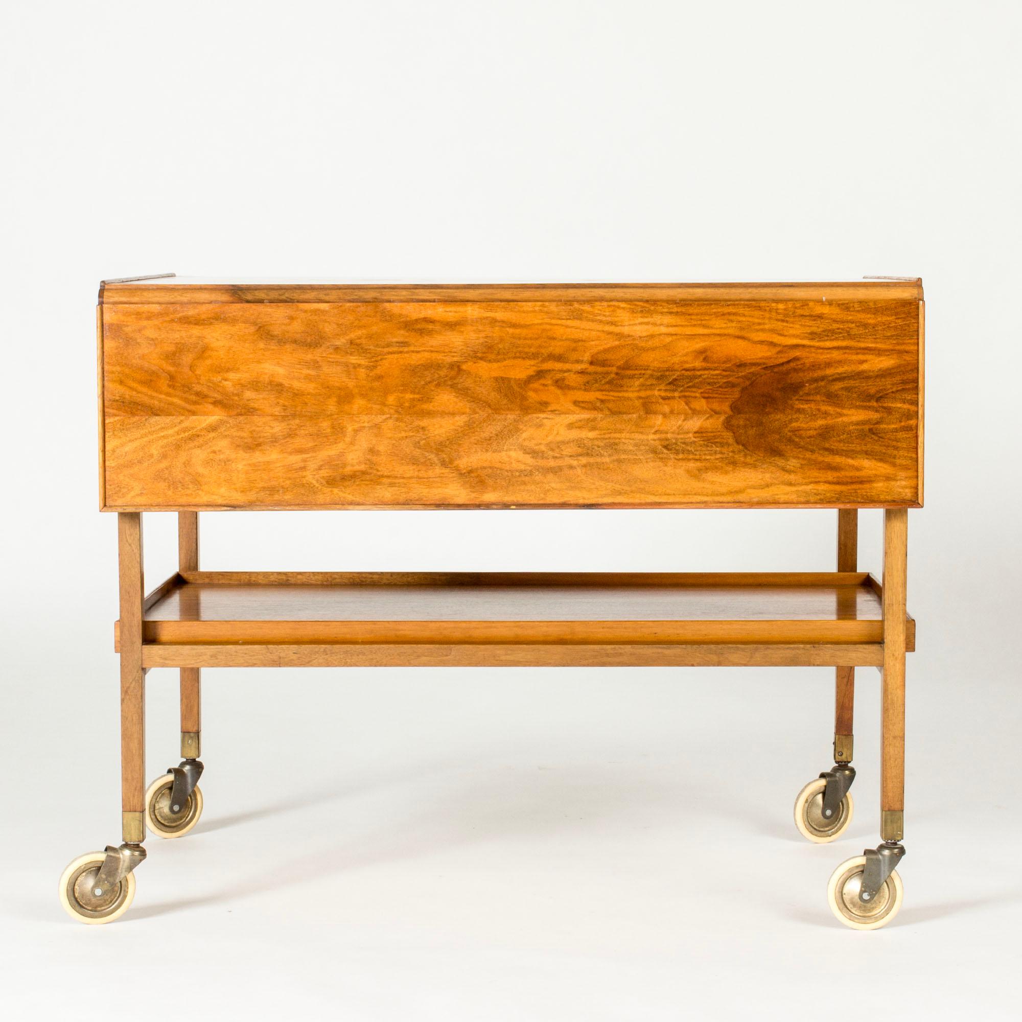 Elegante carrello da portata di Josef Frank, realizzato in mogano con un design versatile. Un'anta a ribalta, un cassetto che scorre in entrambi i sensi e un vassoio rimovibile sotto il piano del tavolo.

Larghezza 89 cm con le ante estese.
