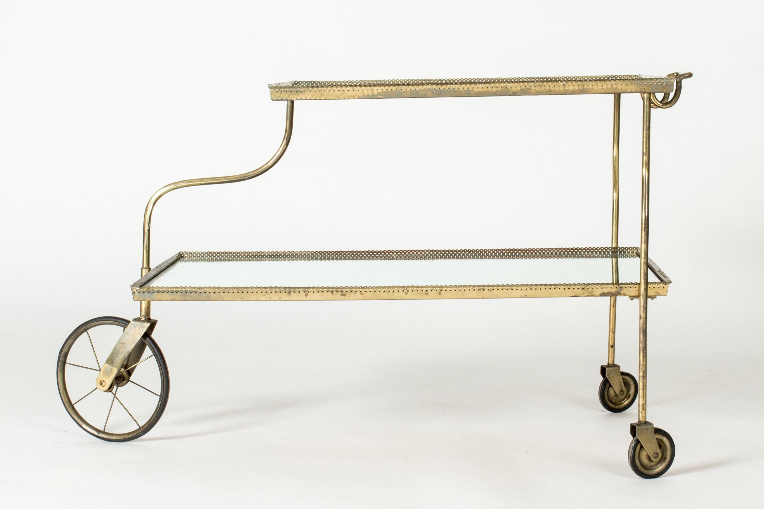 Elegant mirrored glass bar trolley on wheels by Josef Frank, made with a brass frame. The frame has a scalloped edge with a perforated pattern. Clean and decorative design.
