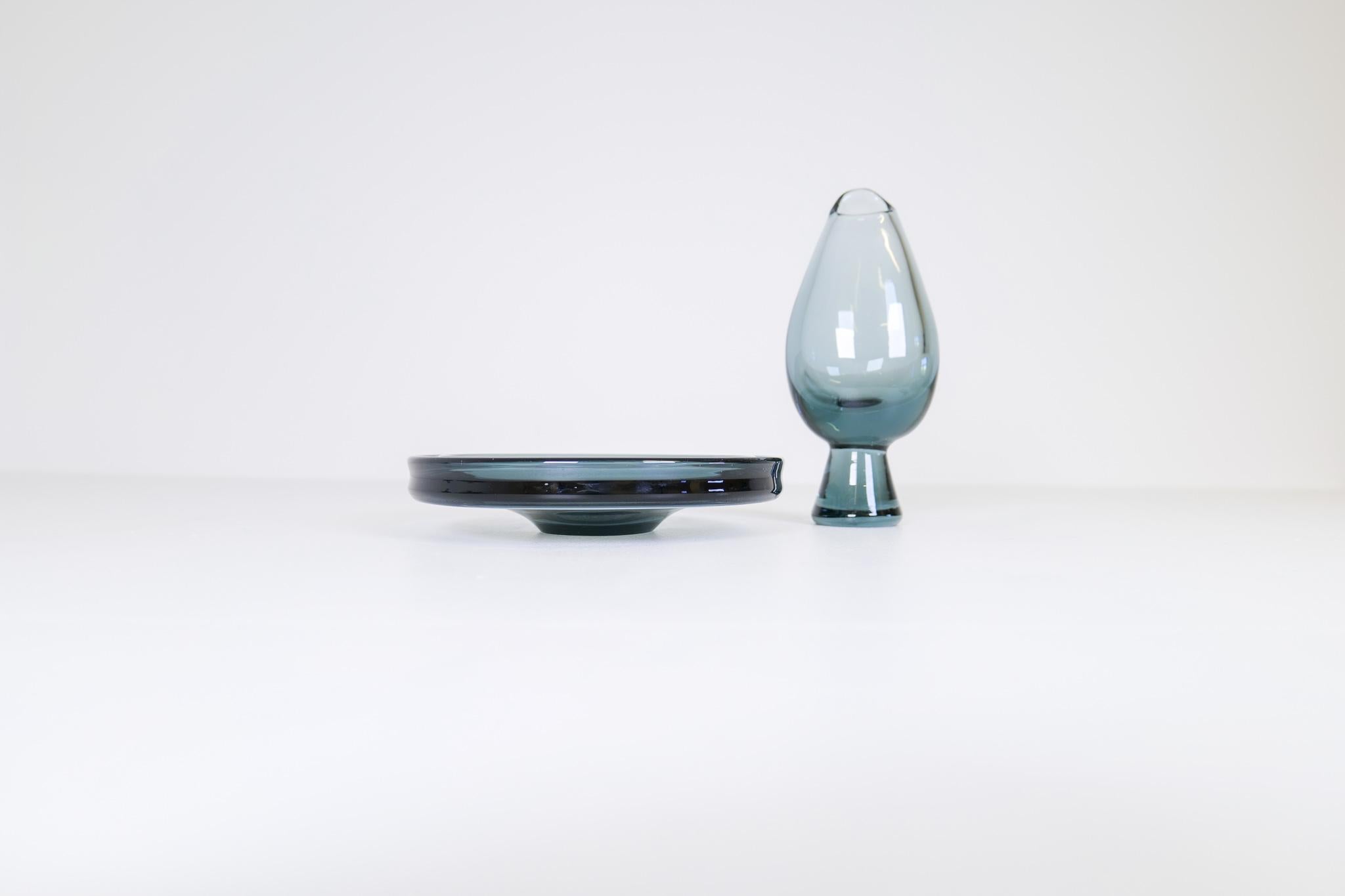 Diese beiden Gefäße, eine Vase und ein Glasteller, wurden von Vicke Lindstrand und Göran Wärff für Kosta Sweden entworfen. Sie haben schöne Linien, die perfekt mit seiner blau getönten Farbe funktioniert. 

Schöner Zustand mit einigen