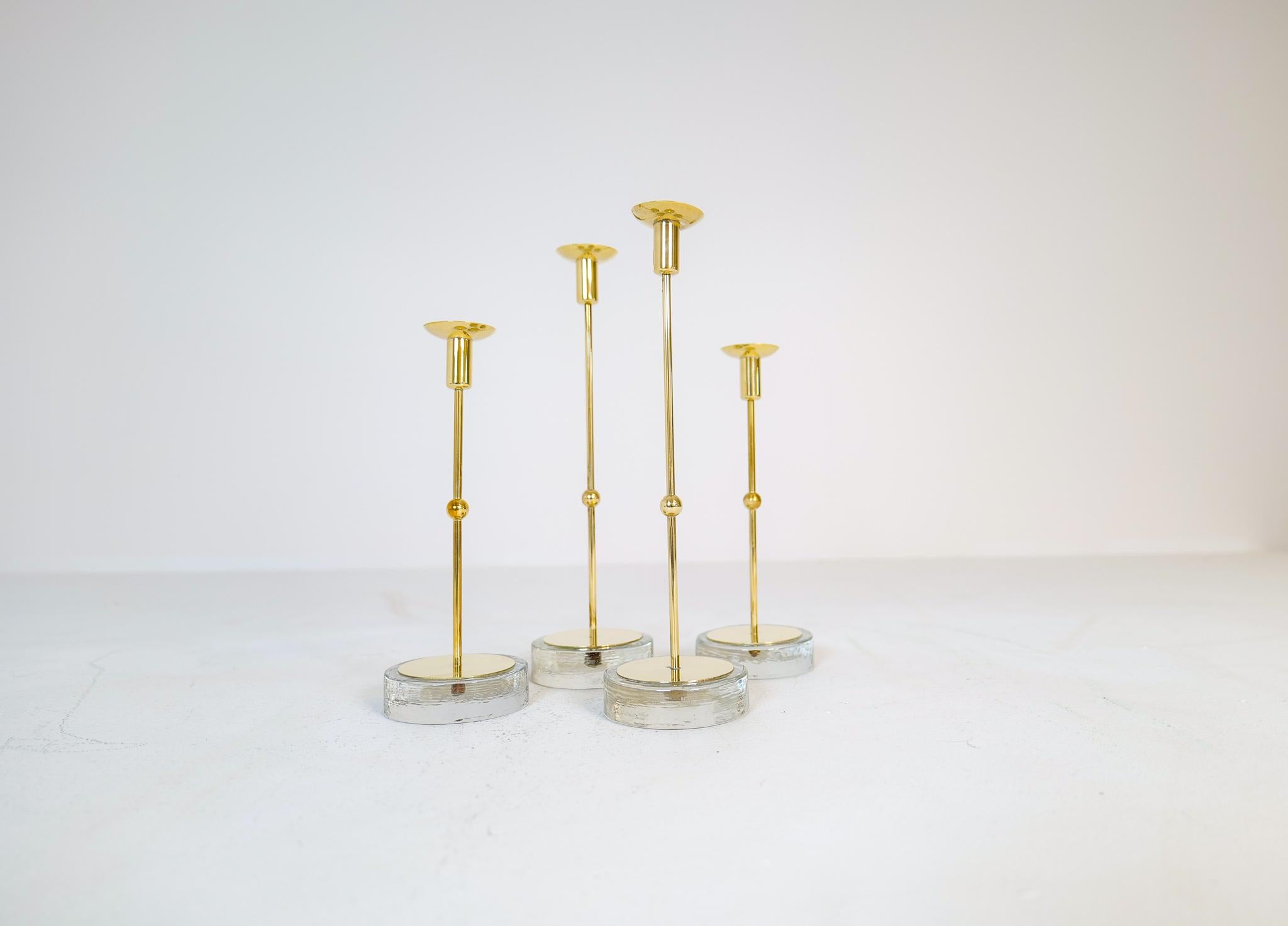 This set of 4 candleholder was designed in Sweden at Ystad Metall and by Gunnar Ander in the 1950s. 
The base is made of glass and the holder in brass. The pieces give that look of Swedish modern design. They are made to hold small candles and are