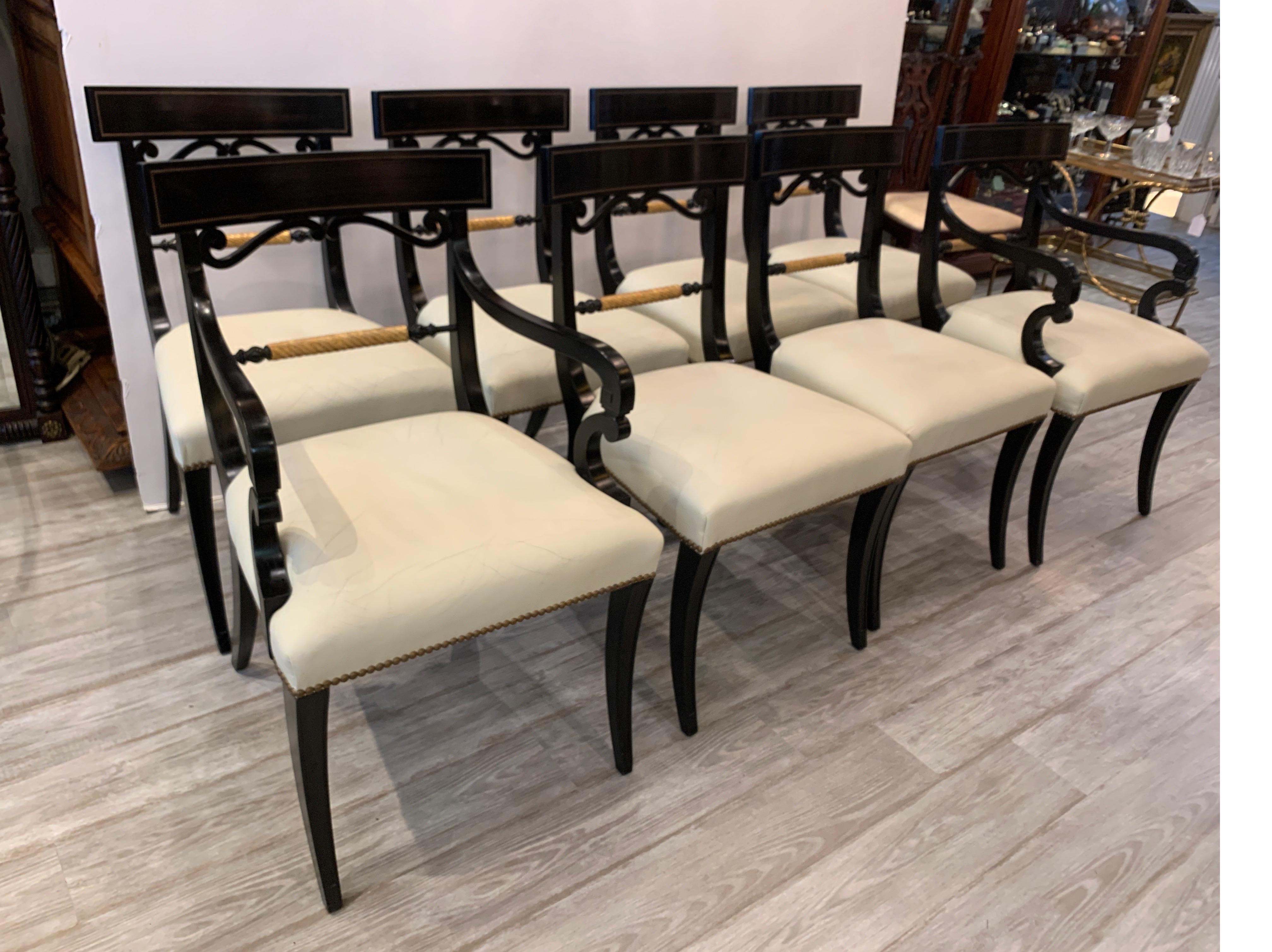 Elegant set of eight Regency style dining chairs, ebonized with gold gilt highlights and original cream leather seats. Brass nailhead trim and elegantly curved and tapered legs give this set of two arm chairs and six side chairs a distinguished