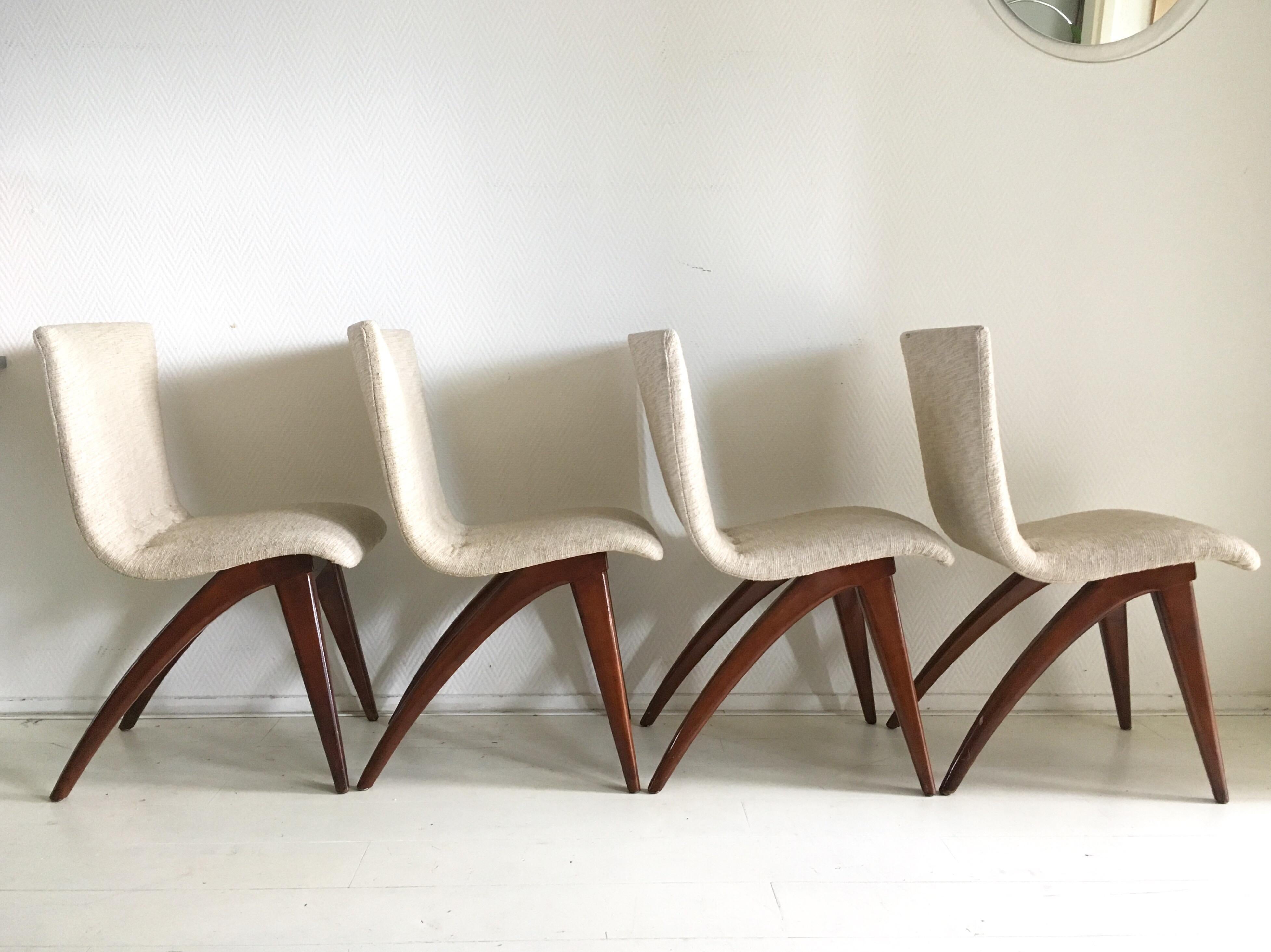 Wonderful sculptural set consisting of four chairs with brown lacquered wooden legs and a flexible, comfortable seating upholstered with off-white/cream colored fabric. All of the chairs remain in very good and sturdy however one chair has a small