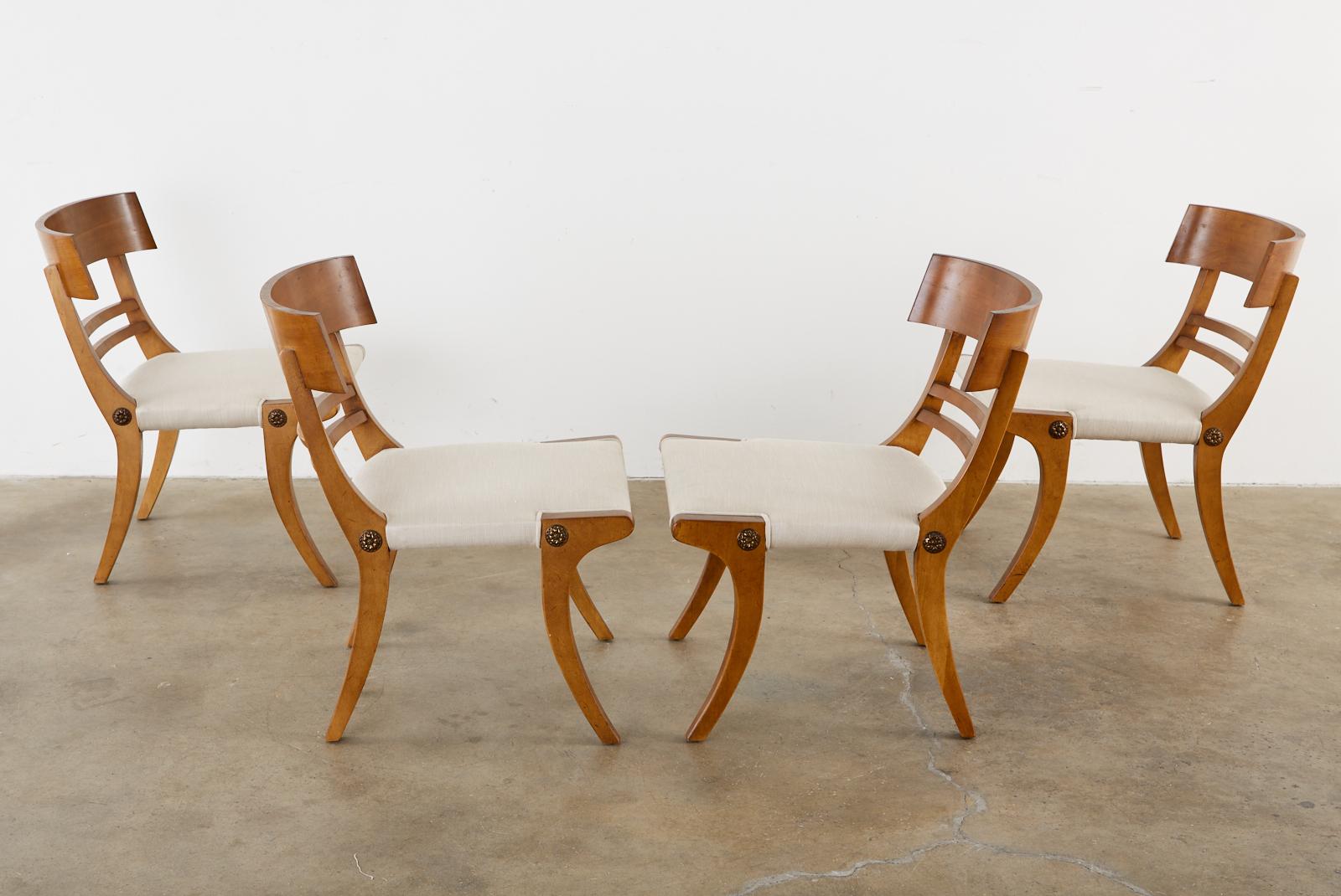 Stylish set of four Mid-Century Modern klismos chairs made in the neoclassical Greco-Roman taste. The chairs have a dramatic profile with a wide curved tablet back support. The seat is supported by distinctive saber legs having a decorative bronze