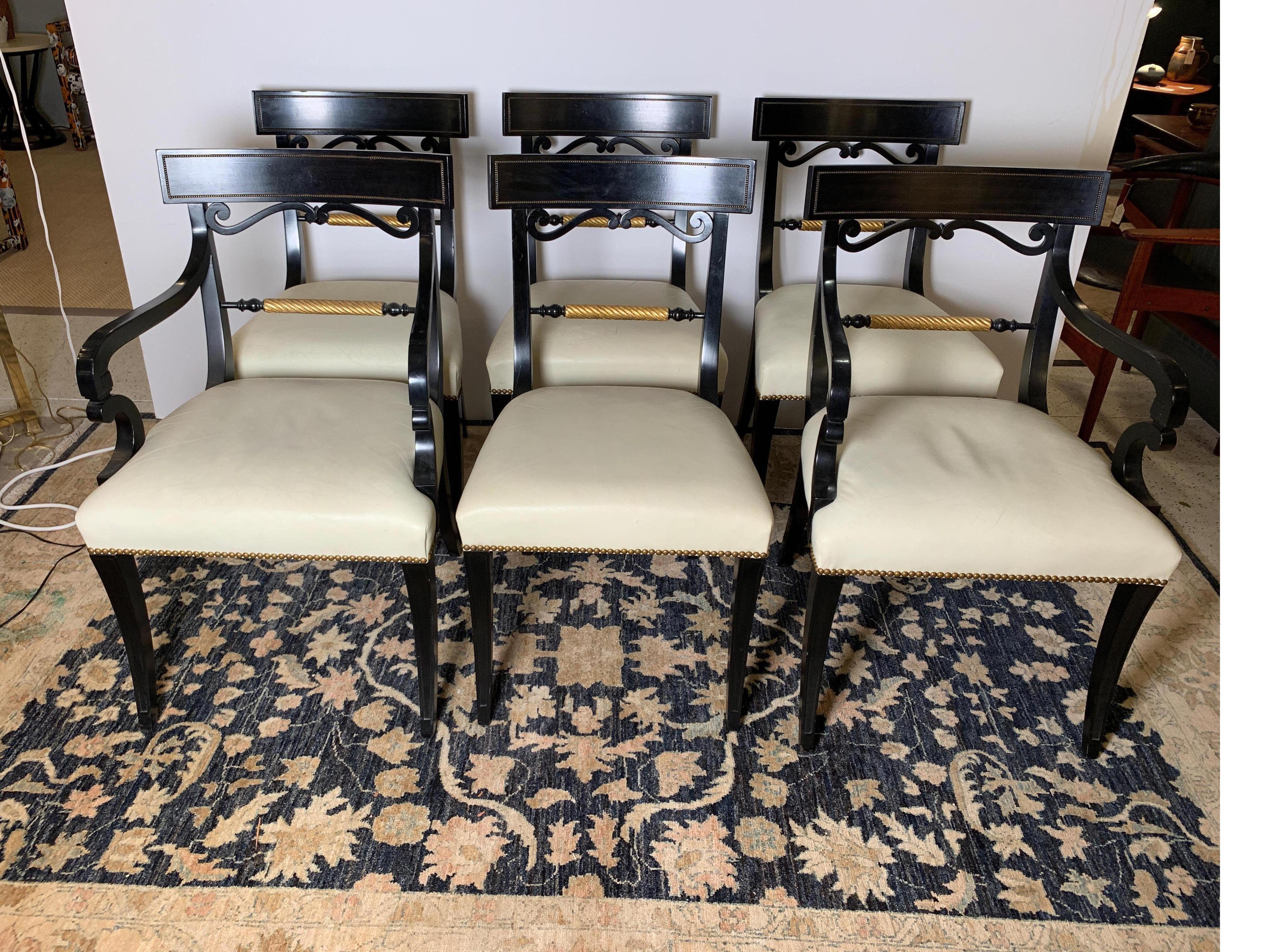 Elegant set of six Regency style dining chairs, ebonized with gold gilt highlights and original cream leather seats. Brass nailhead trim and elegantly curved and tapered legs give this set of two arm chairs and four side chairs a distinguished