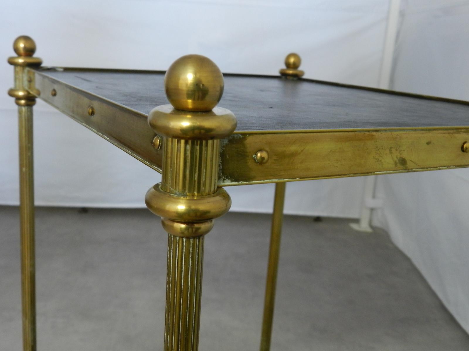 Small side table midcentury two-tier étagère style of Maison Baguès
Black leather tops
Gilt brass finials and fluted legs
Sofa or end table
Good vintage condition one very small old repair to the leather to the edge on the lower tier not very