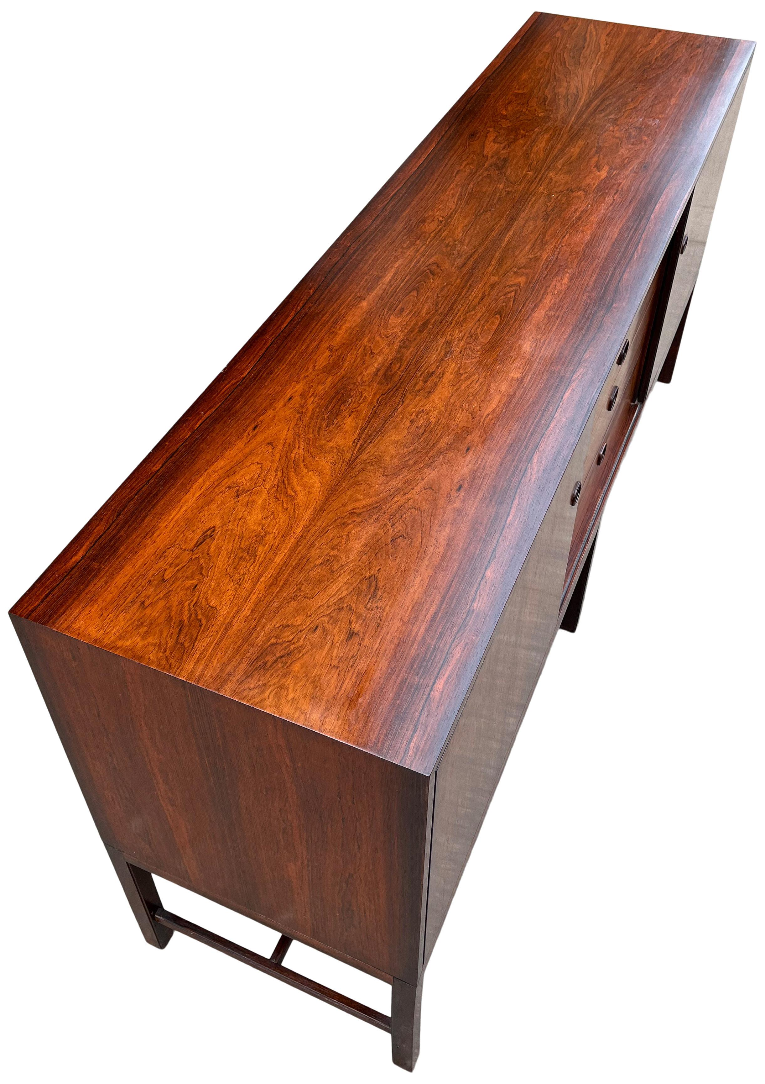 Gorgeous sideboard in Brazilian rosewood with impeccable construction and crantsmanship. Solid wood floating base. Sliding doors reveal two section with adjustable shelves. Center having pull out drawers. Designed by Kai Lyngfeldt Larsen, a John