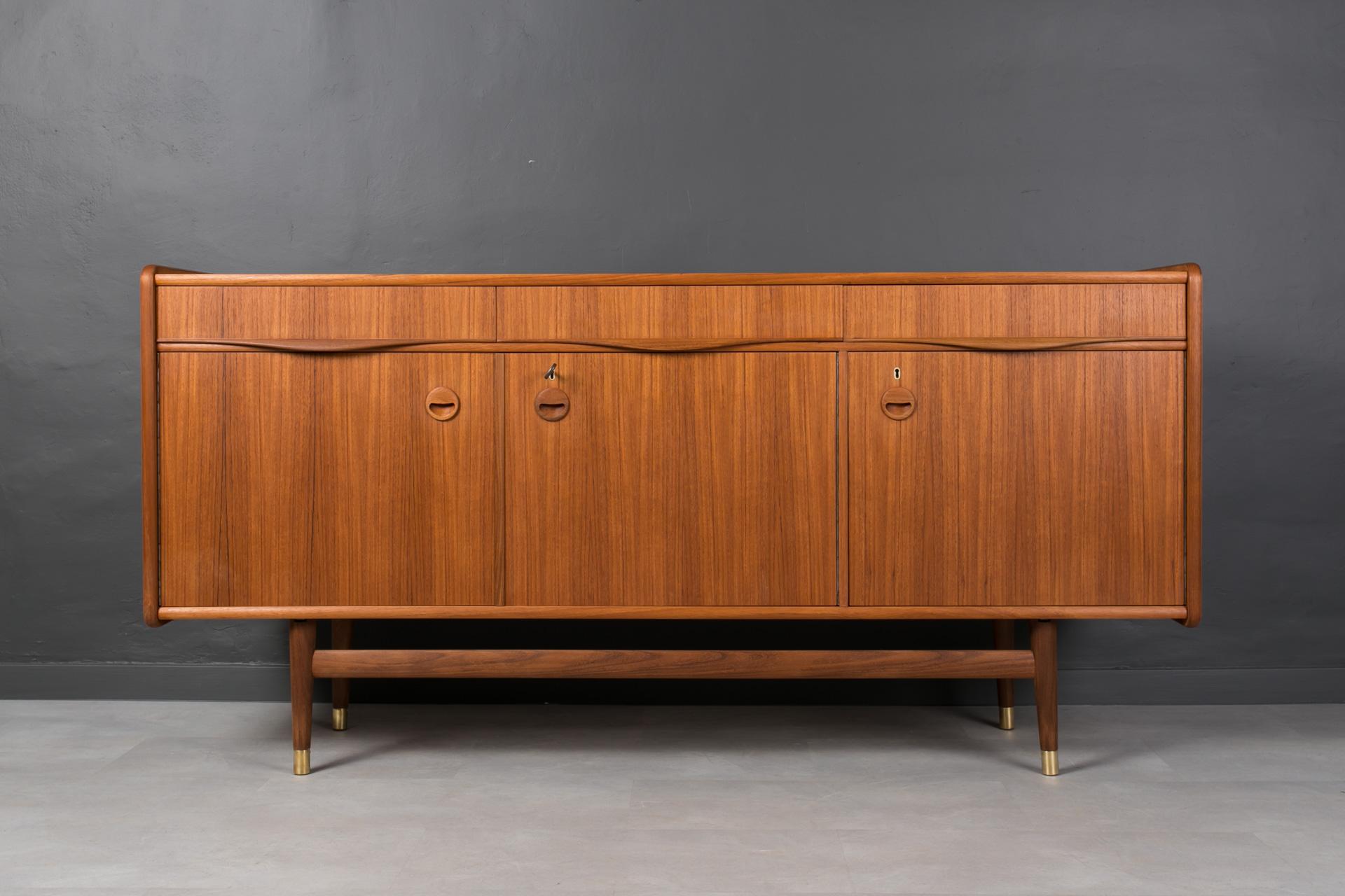This teak sideboard comes from Norway and was made around 1960s. It is most probably one of Sven Andersen designs. It features two storage sections, each one with a shelf. Both sections are lockable with a key. Three practical drawers reside above