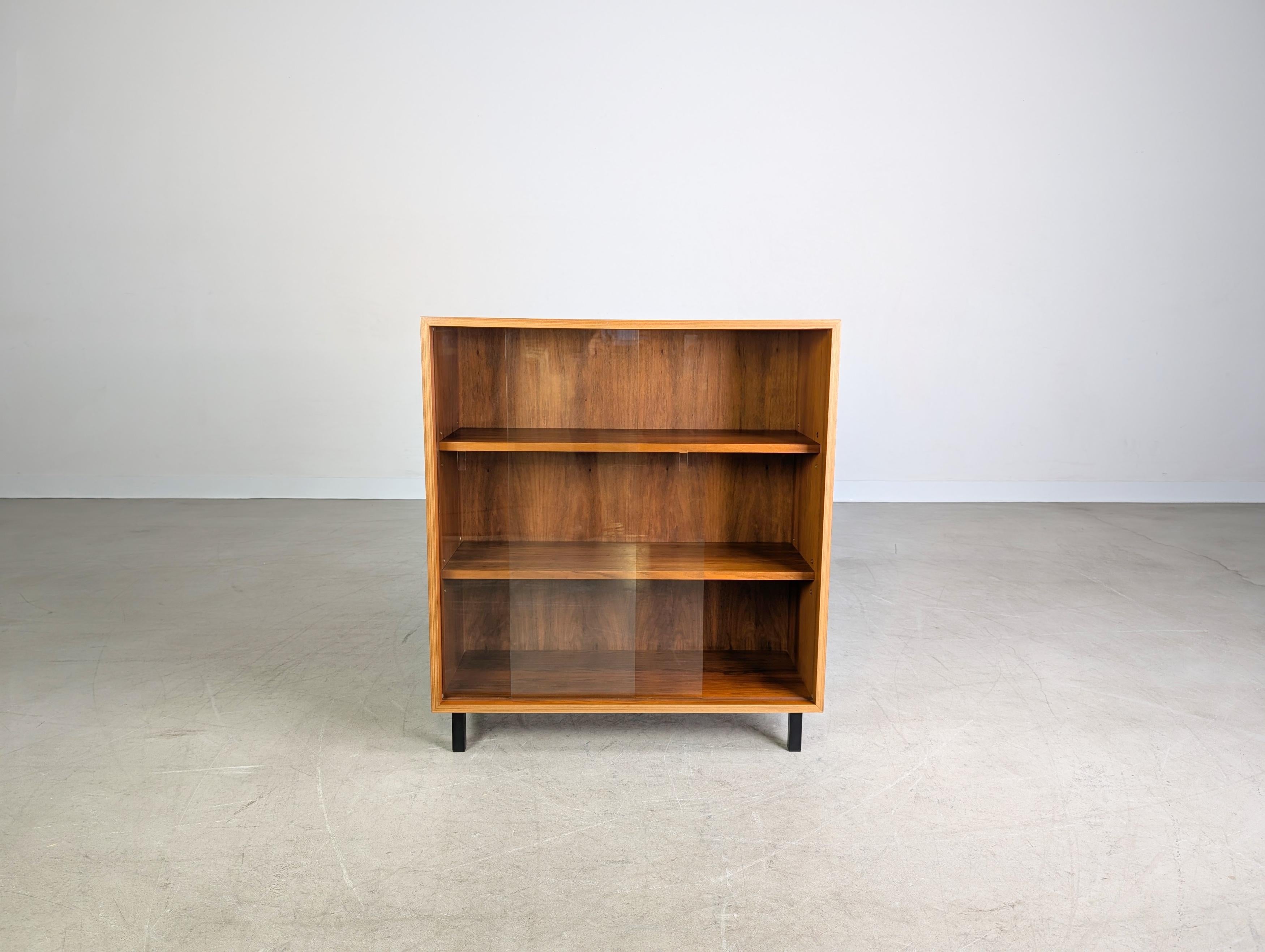 Wir bieten eine hochwertige kleine Vitrine aus Nussbaumholz aus den 1960er Jahren zum Verkauf an. Das Möbel verfügt über zwei Glasschiebetüren und lässt sich aufgrund seiner minimalistischen Formgebung sehr gut auch in moderne Wohnräume