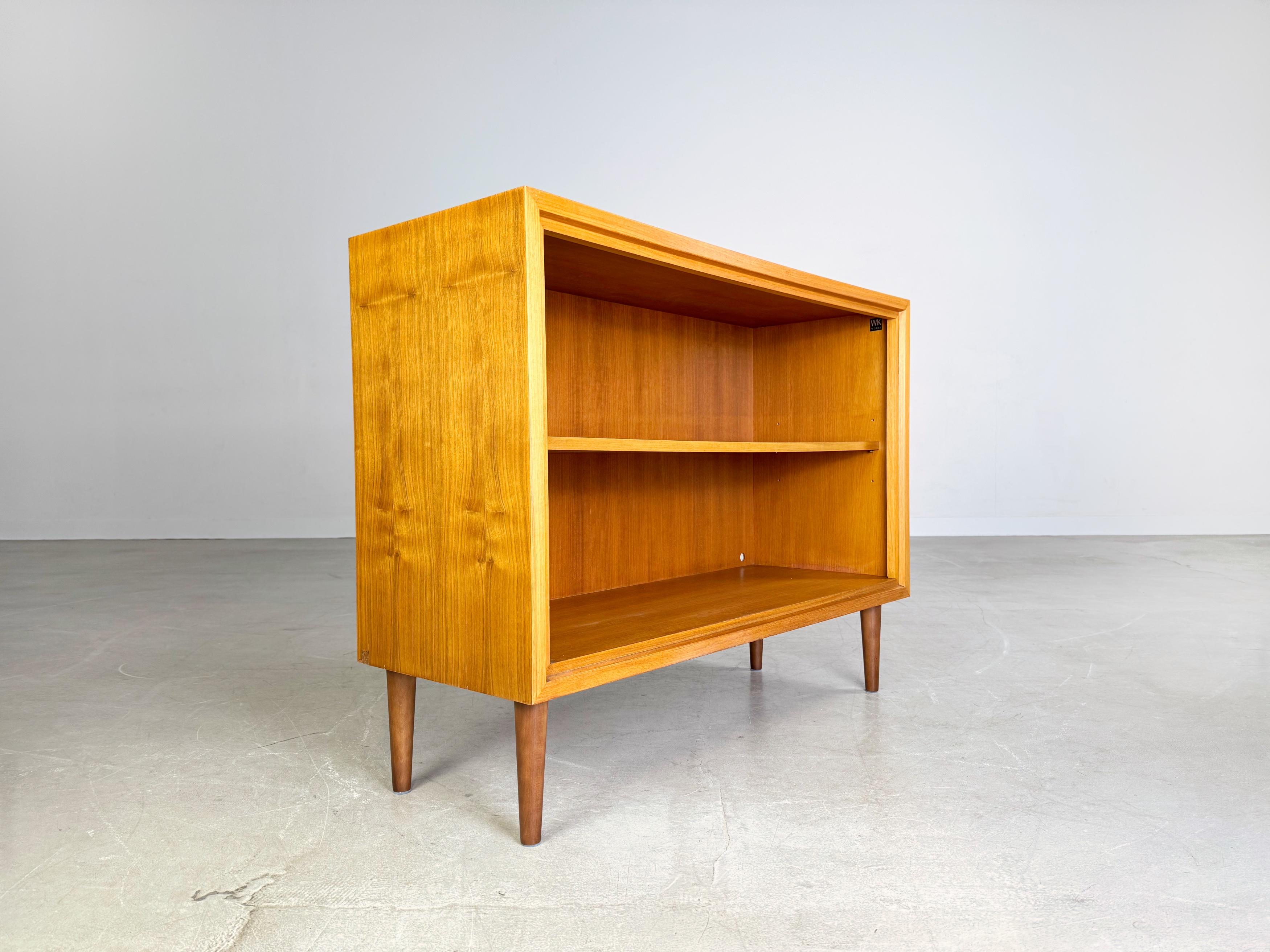 Wir bieten ein wunderschönes kleines WK Möbel Sideboard aus den 1960er Jahren zum Verkauf an. Das Sideboard verfügt über zwei Türen und wurde aus hochwertigem Nussbaumholz gefertigt. Die vier Füße sind aus gebeiztem Buchenholz und nachträglich
