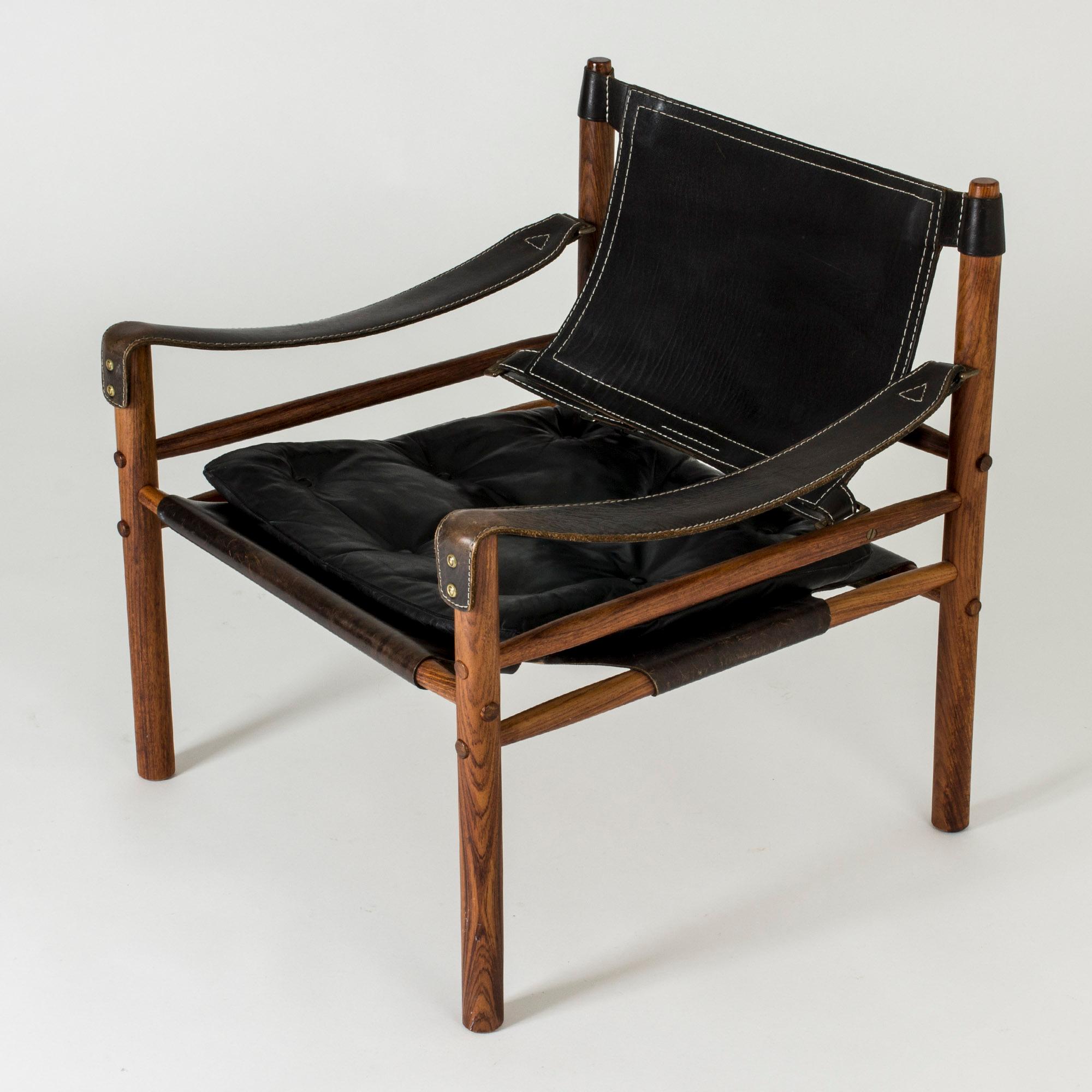 “Sirocco” lounge chair by Arne Norell. Rosewood frame and black leather upholstery, with a removable cushion. Great details of wood plugs decorating the screw holes, seams in the leather and brass buckles.