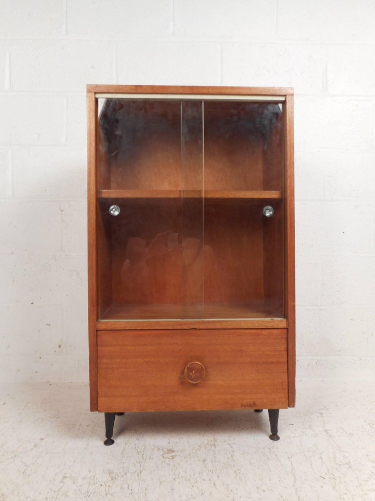 This gorgeous vintage modern cabinet features a hidden drop front compartment on the bottom with a decorative knob. This versatile case piece offers plenty of room for storage and display behind its glass sliding doors. Unique metal recessed pulls