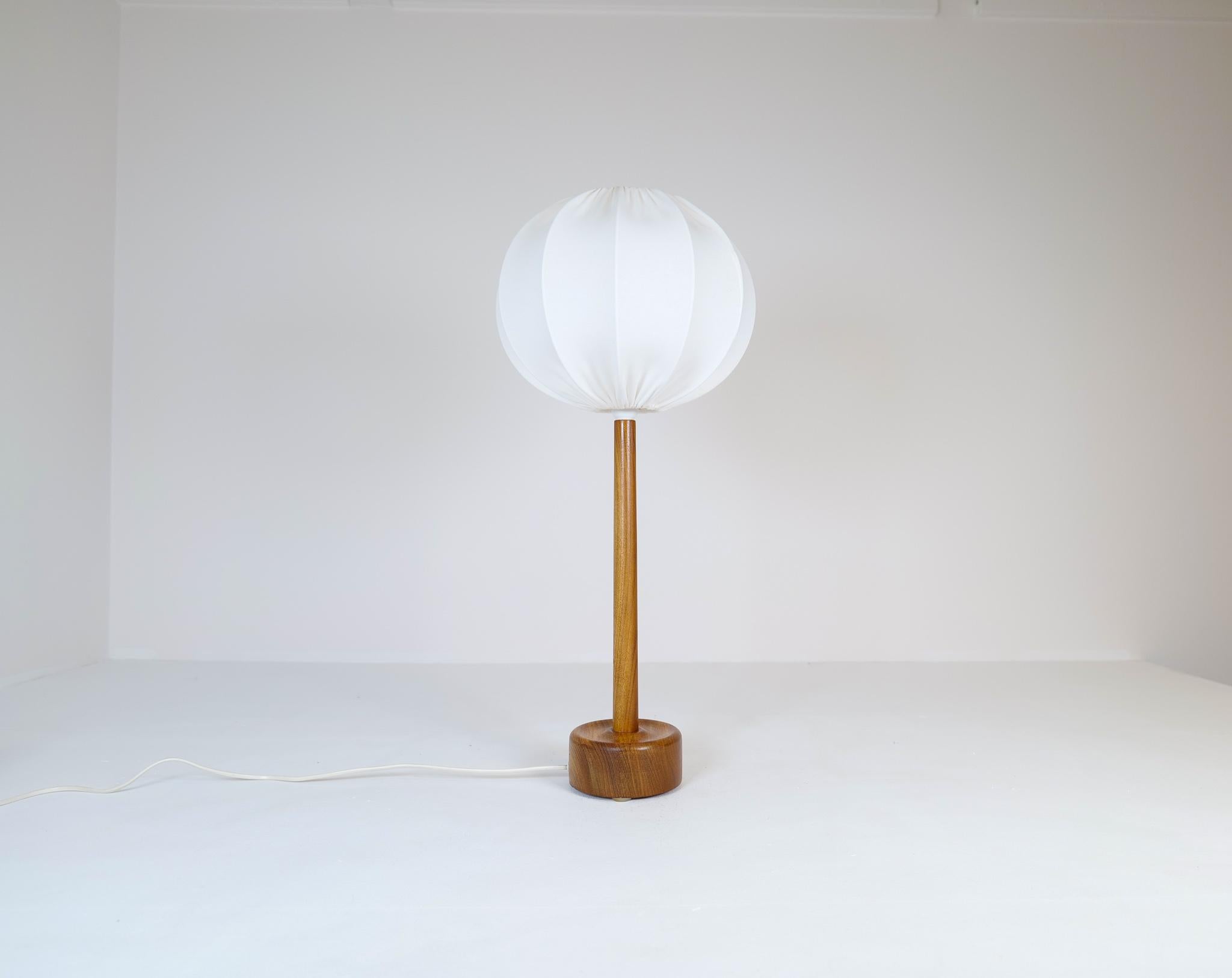 Cette lampe de table en teck massif a été produite en Suède dans les années 1960 et très probablement fabriquée chez Stilarmatur Trans. 
Une base arrondie en teck avec une route élégante en teck qui se termine par un beau nouvel abat-jour donne à