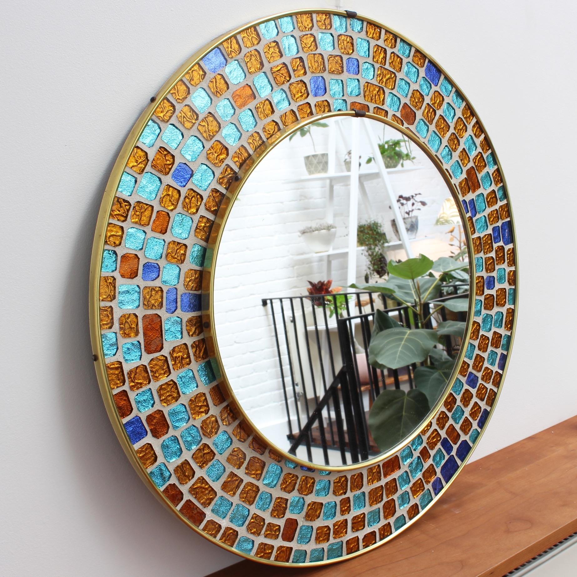 Resplendent midcentury circular brass wall mirror with colorful mosaic surround. Similar in style to Antoni Gaudí's 'Trencadís' technique involving hand-cut-glass tiles in different colors although these are uniform in shape. Spanish origin, circa