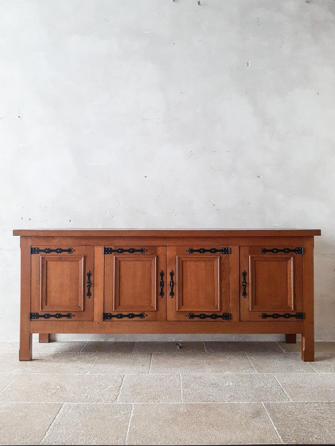 Mid-century Spanish oak credenza. Beautiful Spanish colonial style solid oak sideboard. With four panelled doors and large wrought iron hinges and locks. Behind the four doors a large compartment with a full lenght shelve and two drawers in the