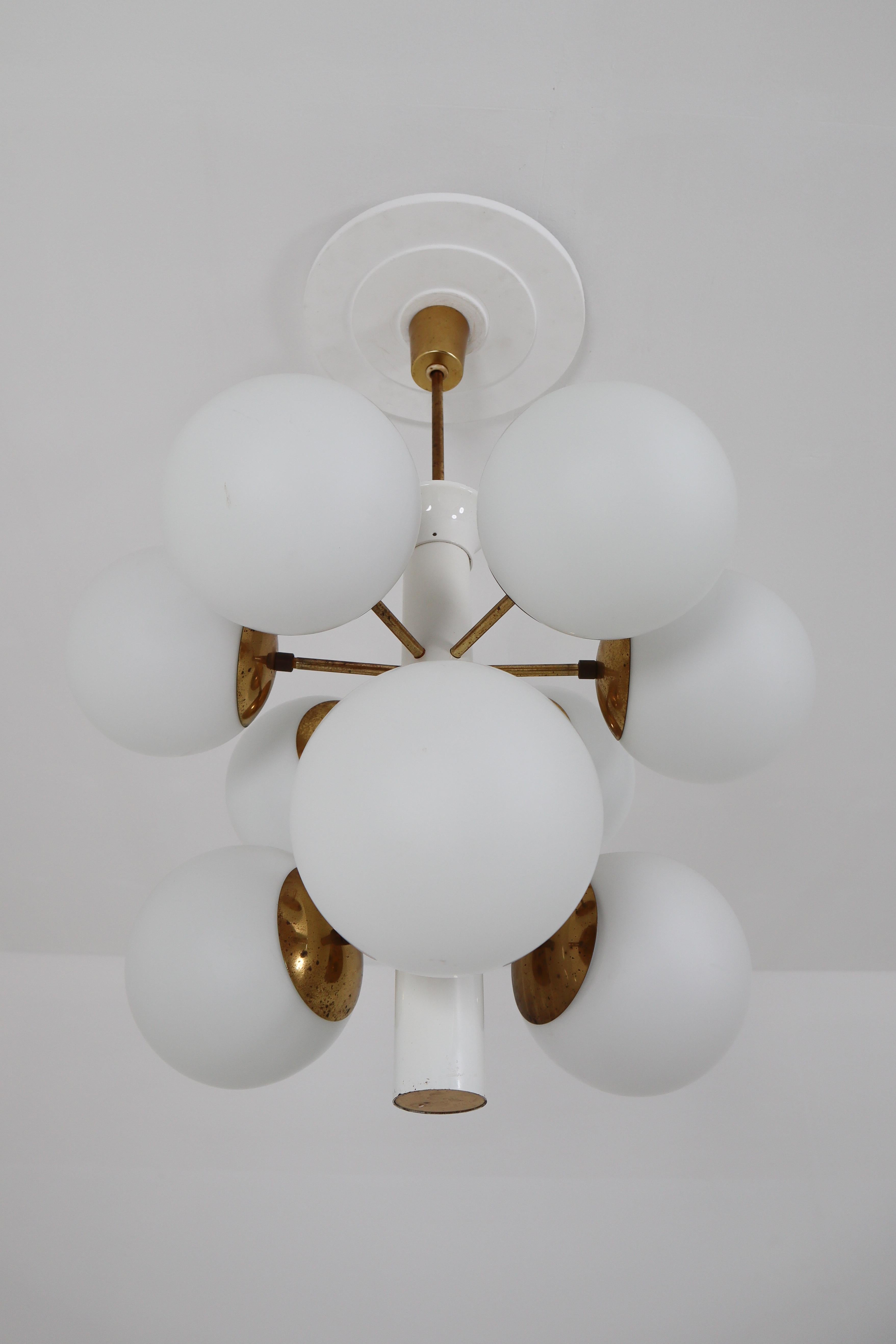This fantastic midcentury Sputnik chandelier was designed in Germany 1960s featuring a patinated brass frame and nine handblown opal glass globes.