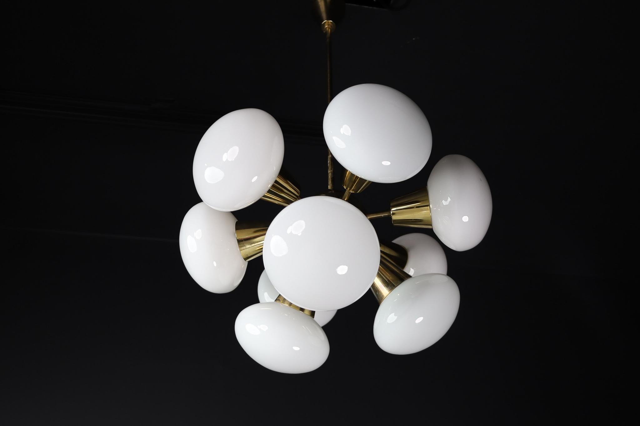 Sputnik chandeliers with brass fixture and Opaline spheres. These chandeliers with brass frame consist of twelve lights. The diffuse light it spreads is very atmospheric. Completed with the opaline glass and brass details, these chandeliers will