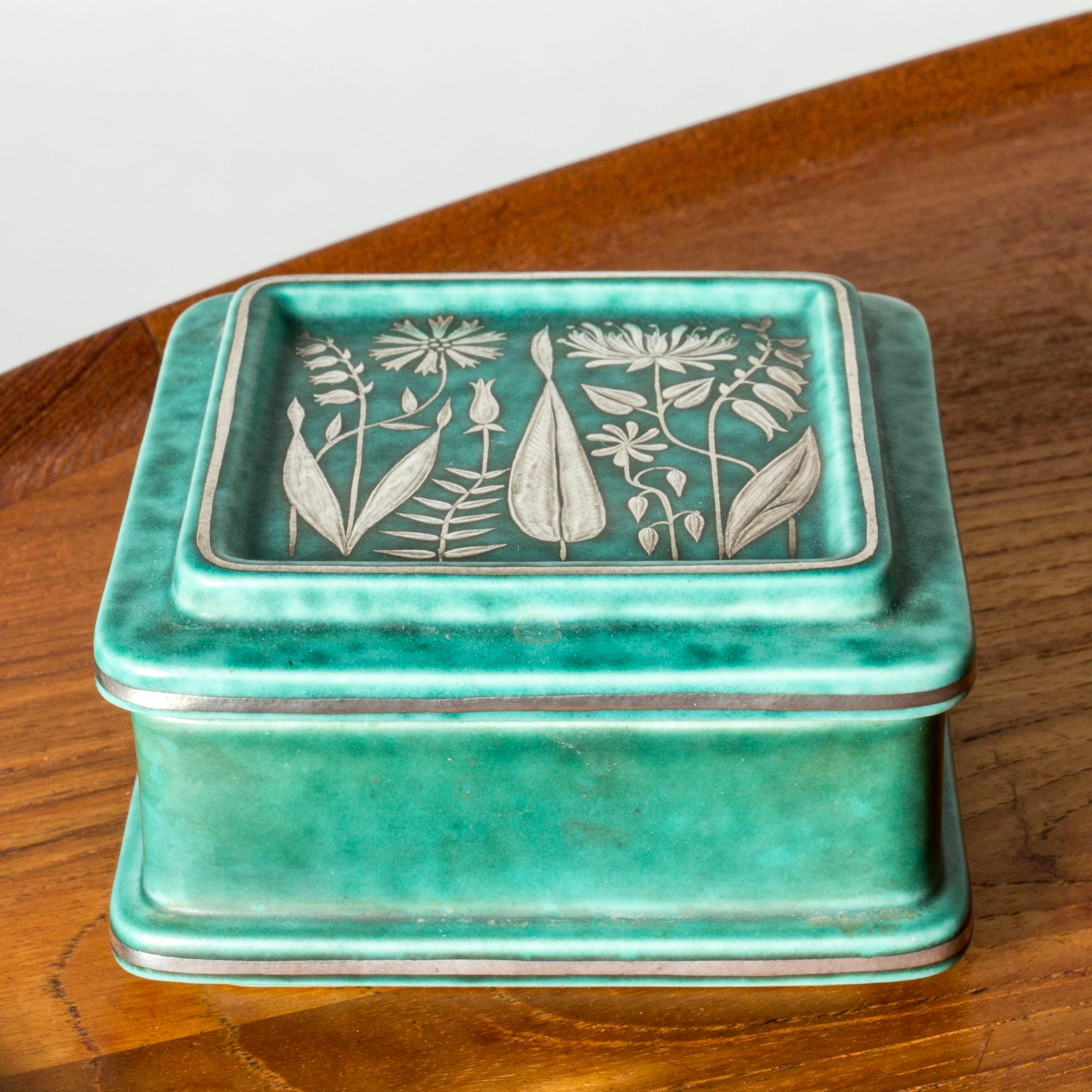 Decorative stoneware “Argenta” box by Wilhelm Kåge in a comfact form. Decorated with a silver leaves and flowers, lovely attention to detail.

“Argenta” was introduced at the Stockholm exhibition in 1930 and became Wilhelm Kåge’s most widely