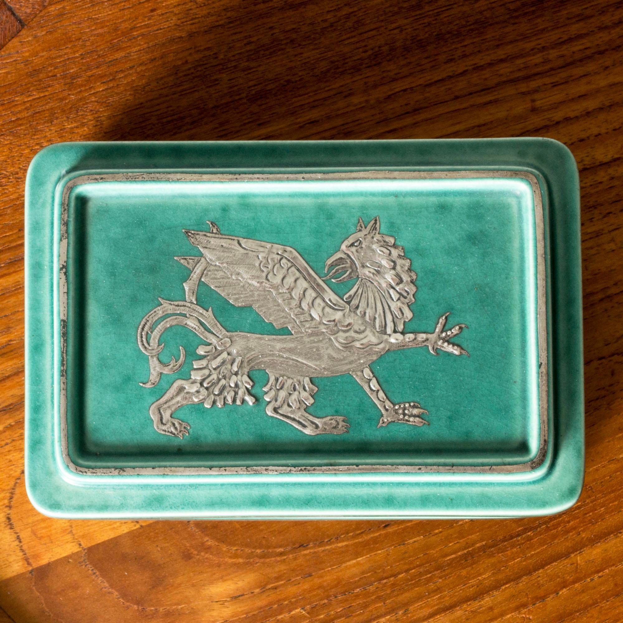 Decorative stoneware “Argenta” box by Wilhelm Kåge in a comfact form. Decorated with a silver griffin, lovely attention to detail.

“Argenta” was introduced at the Stockholm exhibition in 1930 and became Wilhelm Kåge’s most widely appreciated and