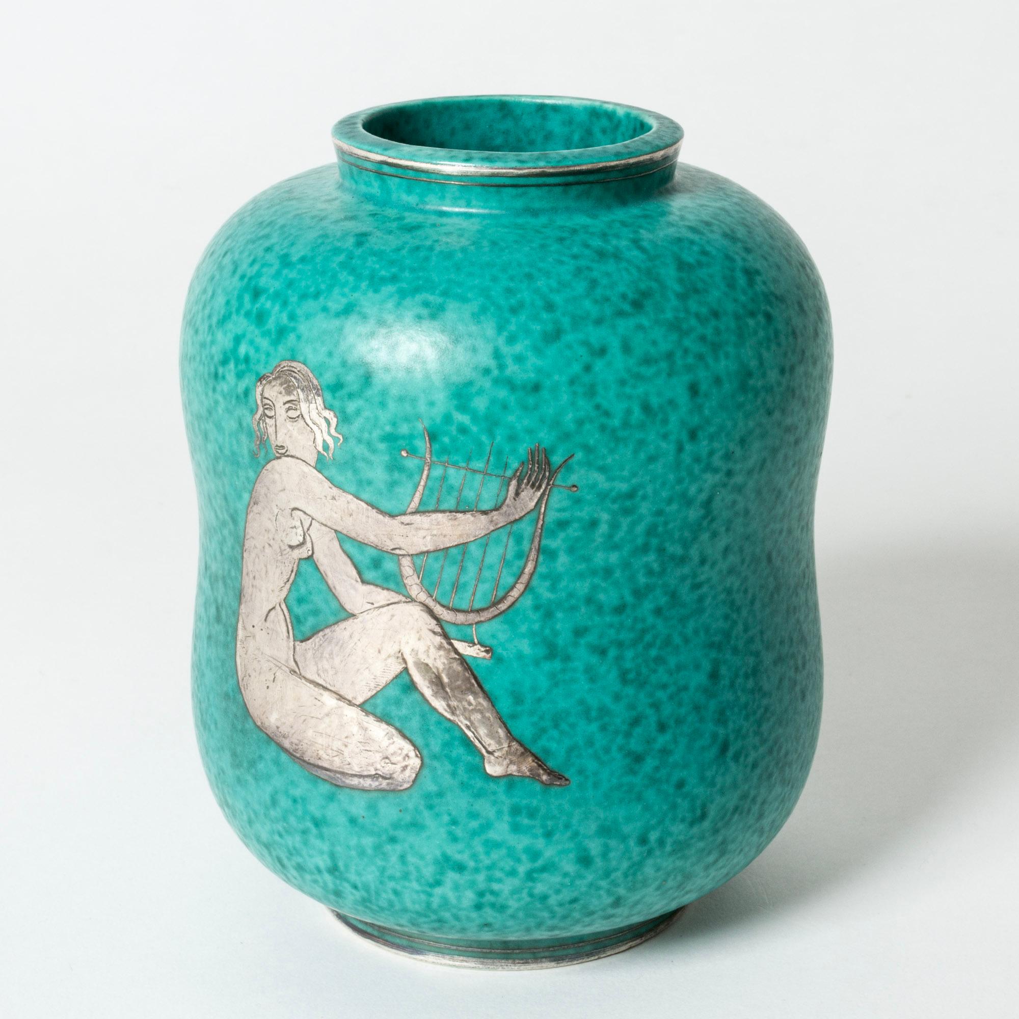 Lovely stoneware “Argenta” vase by Wilhelm Kåge in a curvesome form. Decorated with a motif of a woman playing a harp. Lovely attention to detail.

“Argenta” was introduced at the Stockholm exhibition in 1930 and became Wilhelm Kåge’s most widely